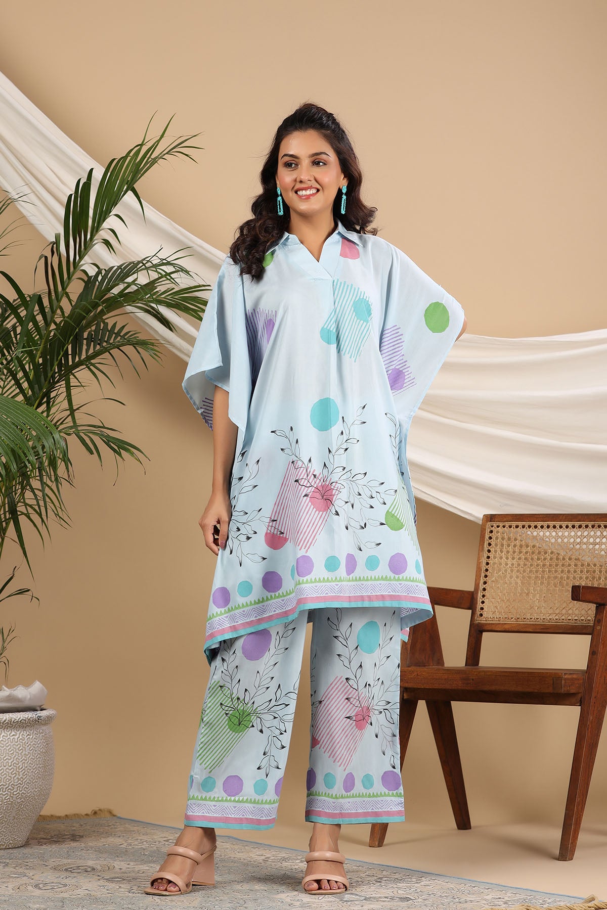 Woman wearing a light blue traditional outfit with colorful patterns in a home setting.