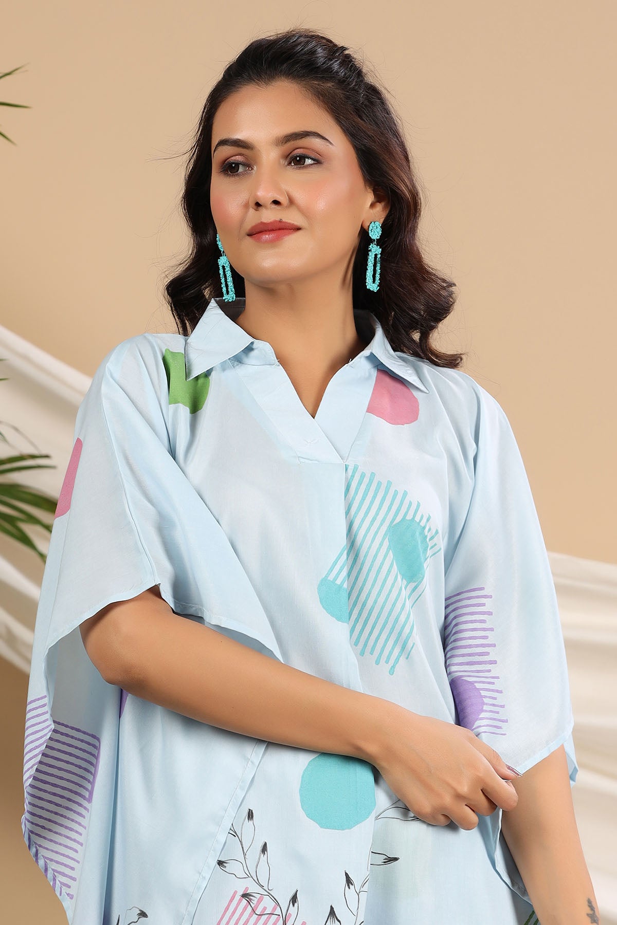 Woman wearing a light blue shirt with colorful patterns against a beige background