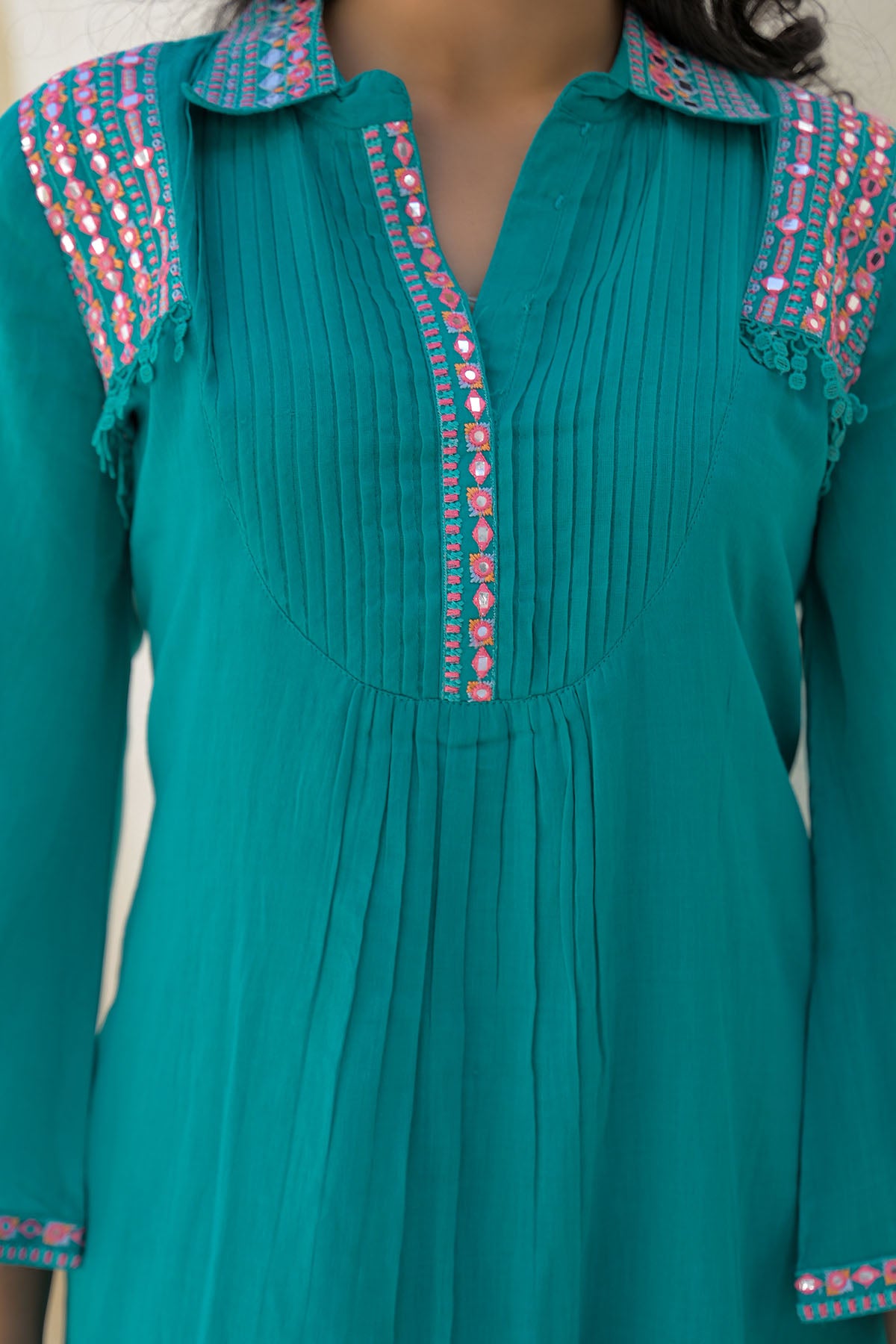 Teal dress with colorful embroidery on a plain background