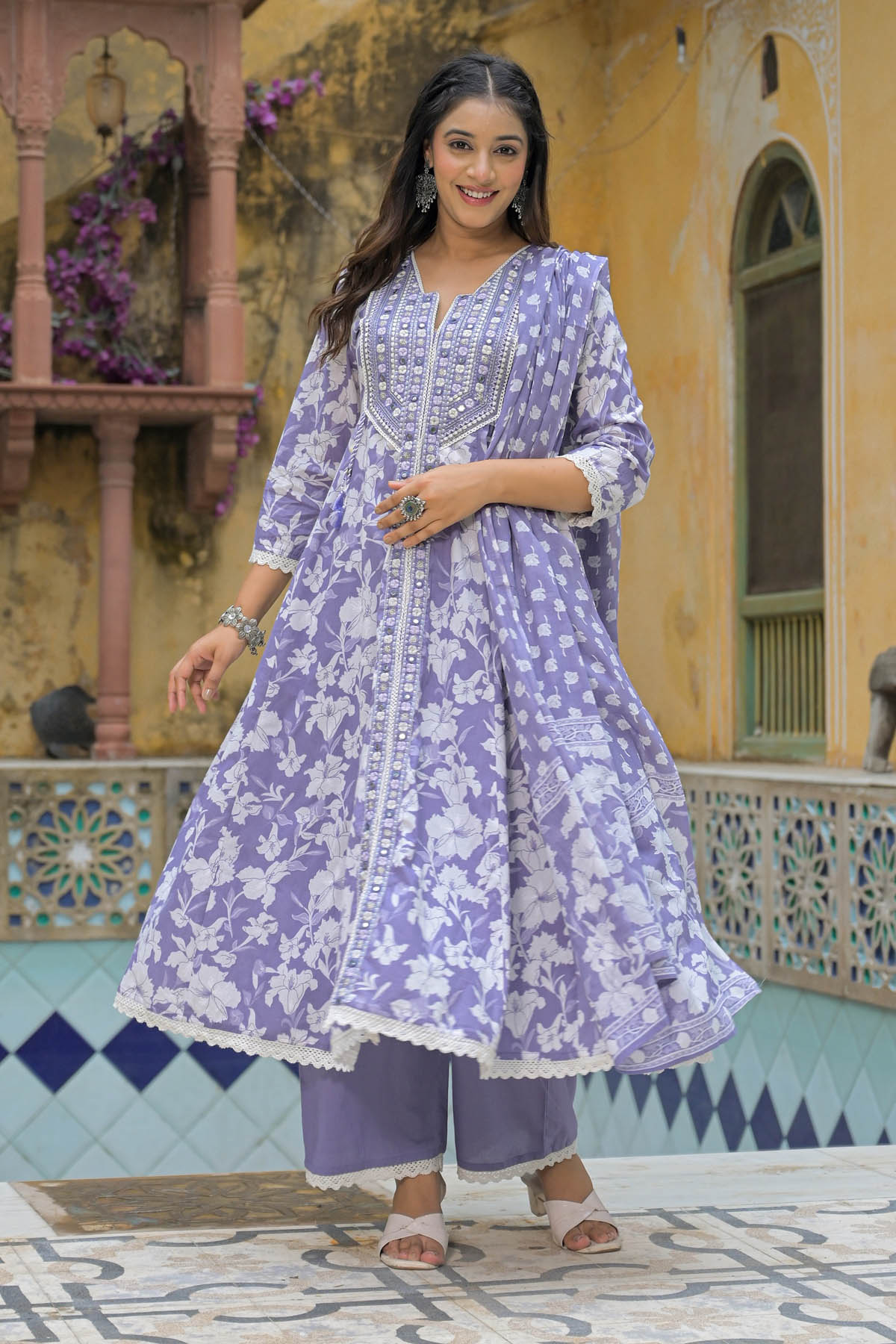 Woman wearing a purple floral outfit standing in front of a decorative building.