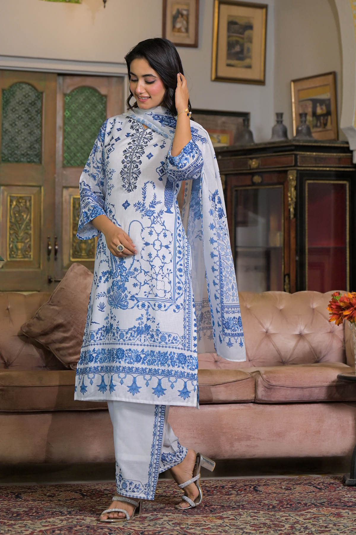 Woman in a blue and white embroidered outfit standing in a living room.