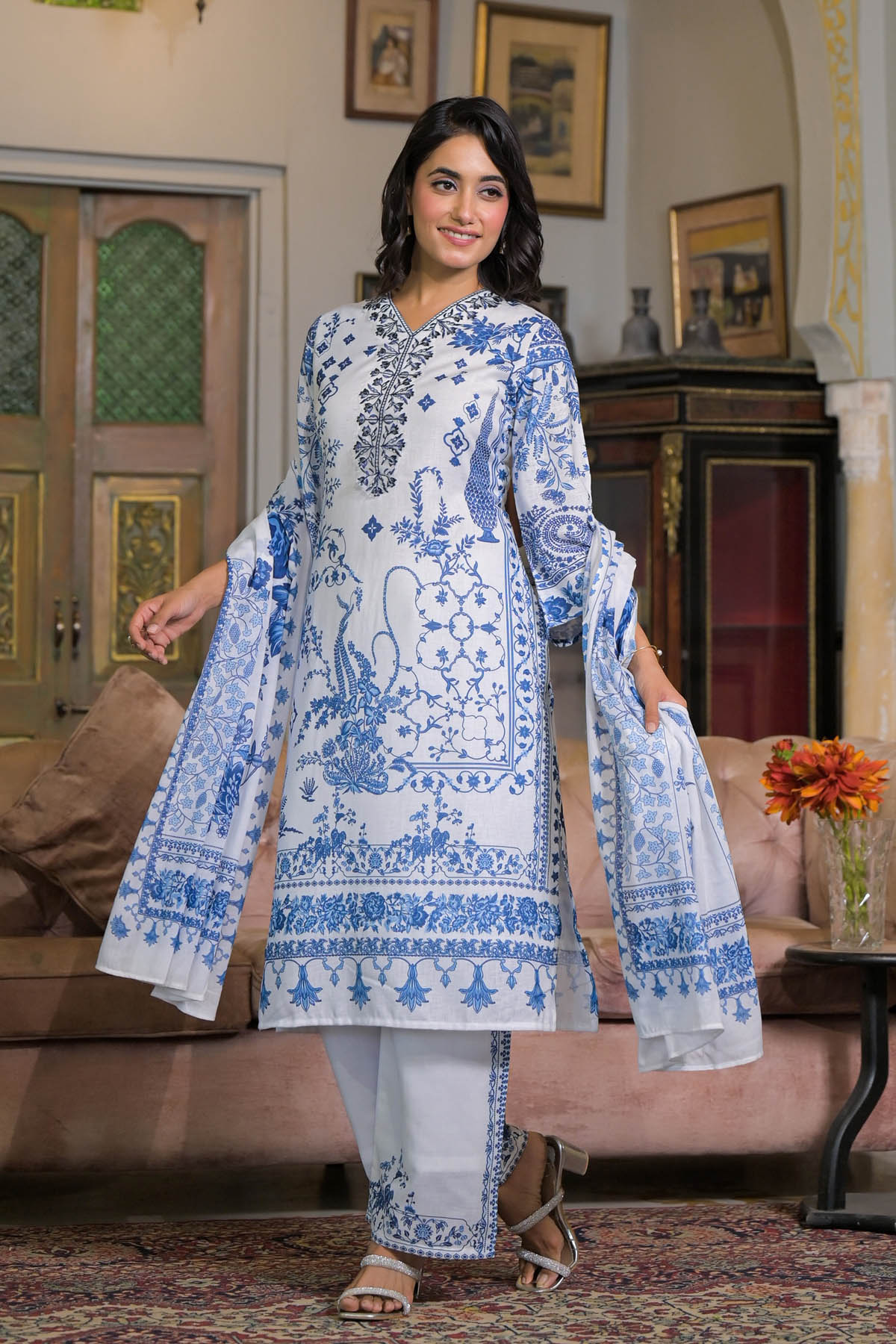 Woman wearing a blue and white embroidered traditional outfit in a decorated room.