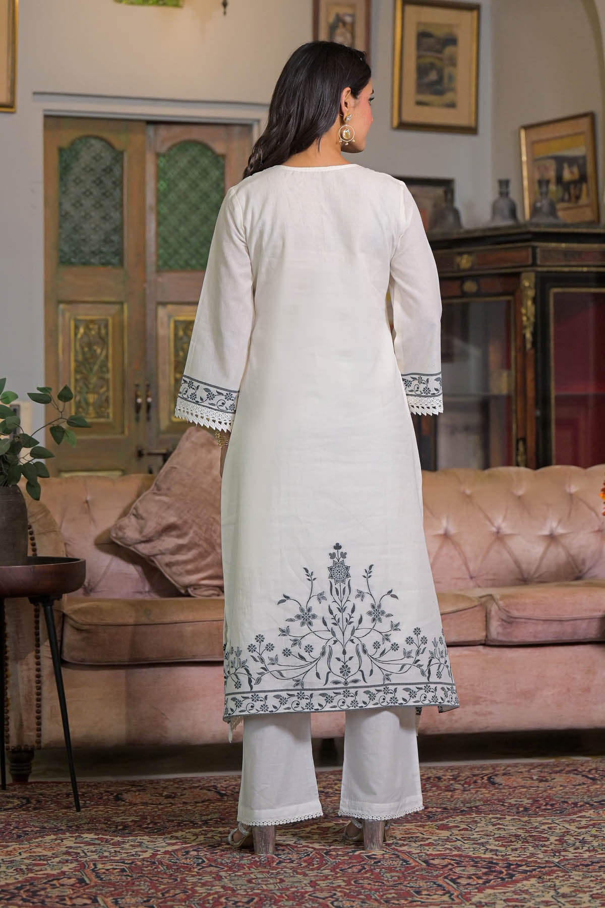 Woman wearing a white kurta with intricate embroidery in a living room setting.
