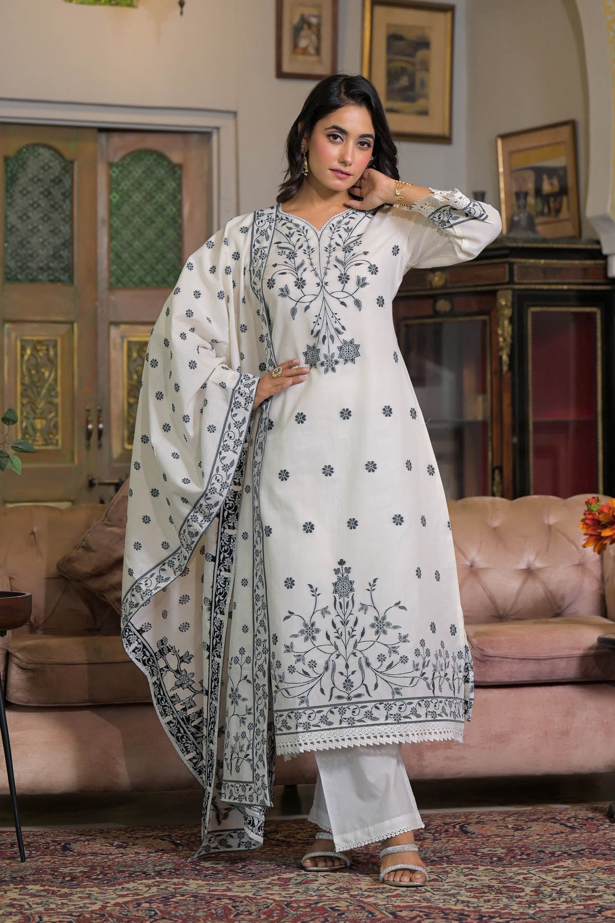 Woman in a white embroidered traditional outfit standing in a decorated room.