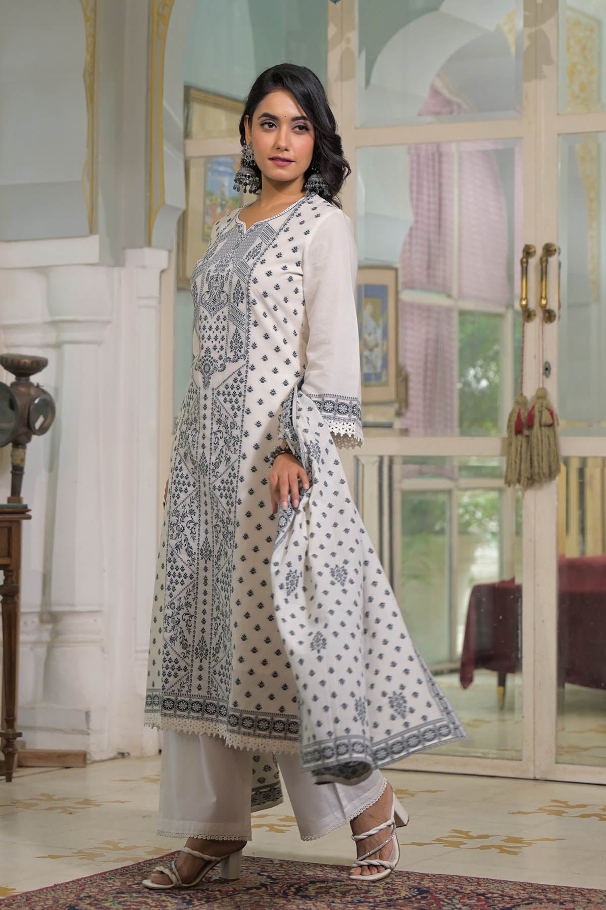 Woman in a white and blue patterned outfit standing in an elegant interior setting.