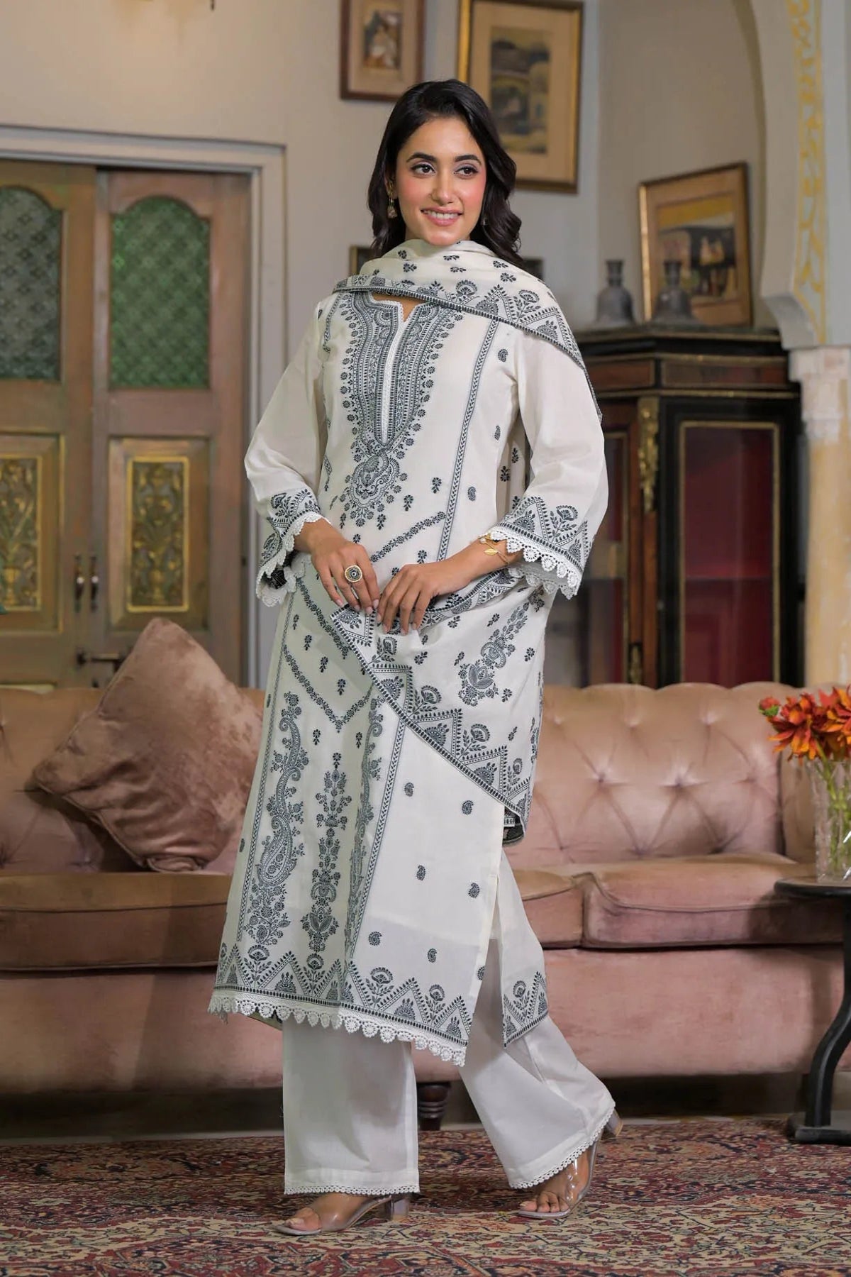 Woman in a white and black embroidered traditional outfit standing in a decorated room.