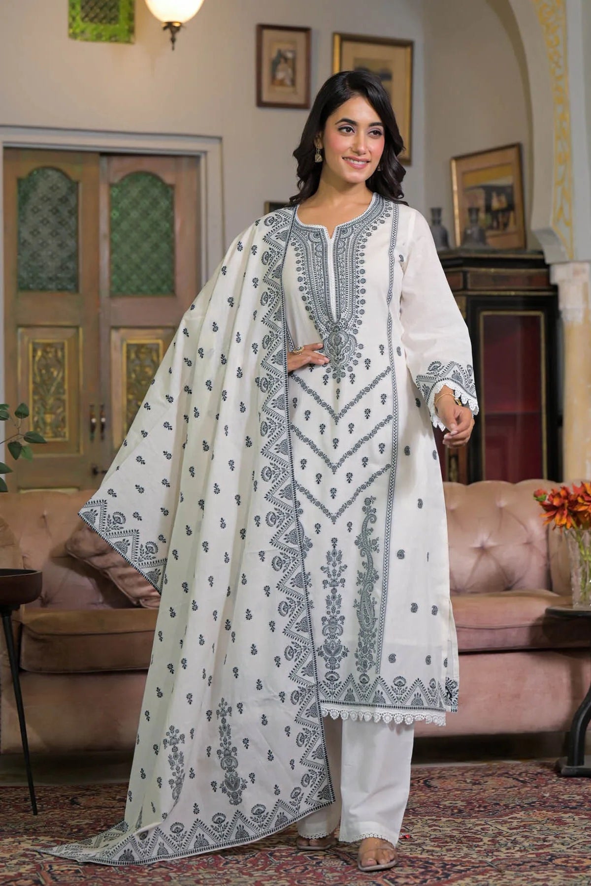 Woman in a traditional white and blue embroidered outfit standing in a decorated room.