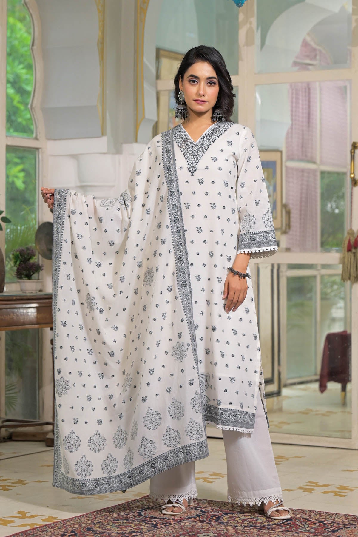 Woman wearing a white and gray traditional outfit in a decorated room.