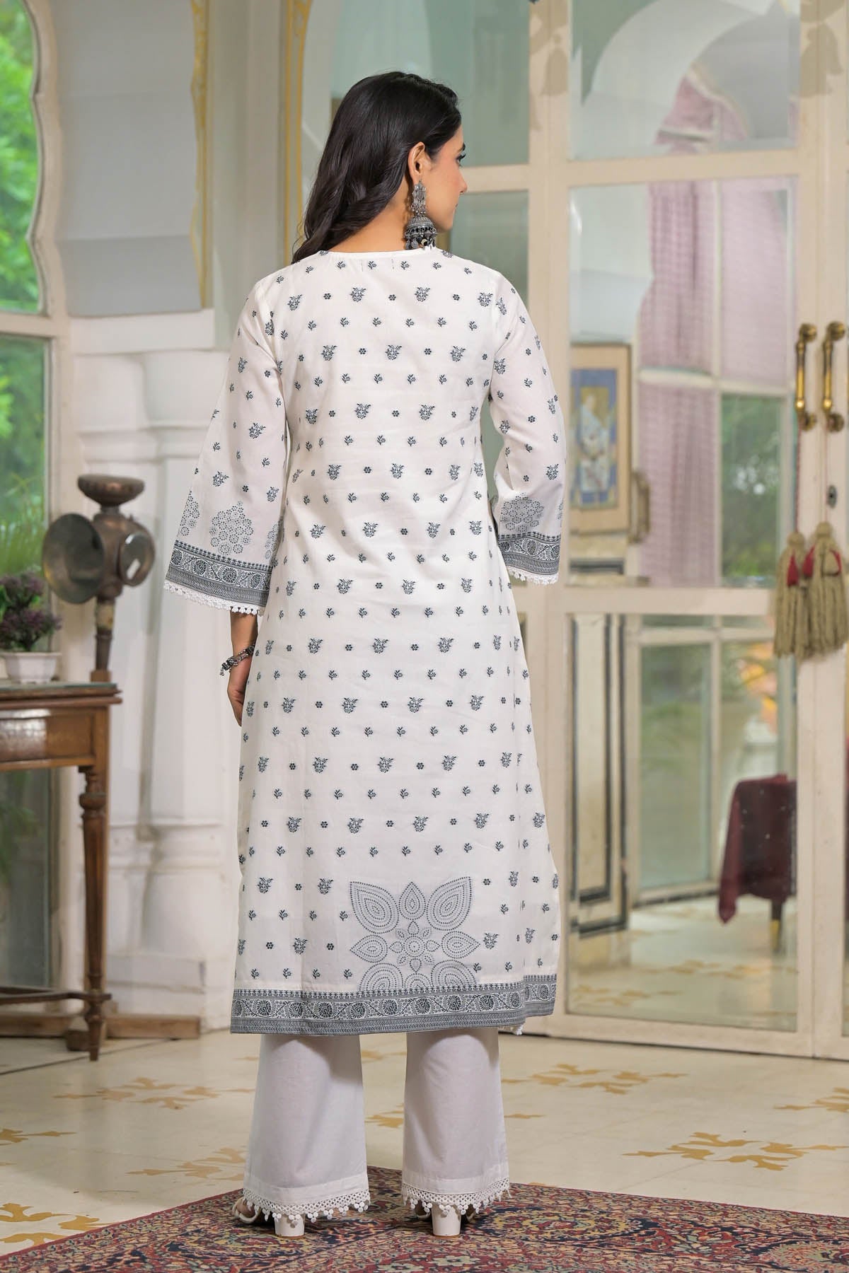 Woman wearing a white kurta with blue patterns in a decorated room.
