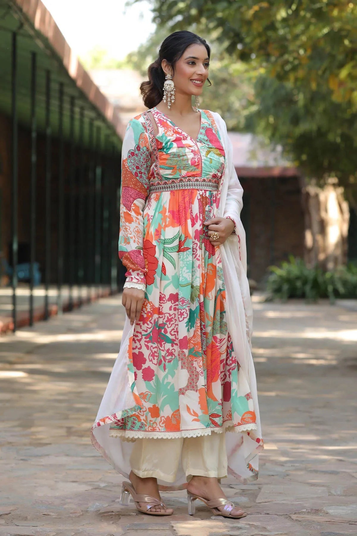 Woman wearing a colorful floral dress with a white dupatta outdoors.