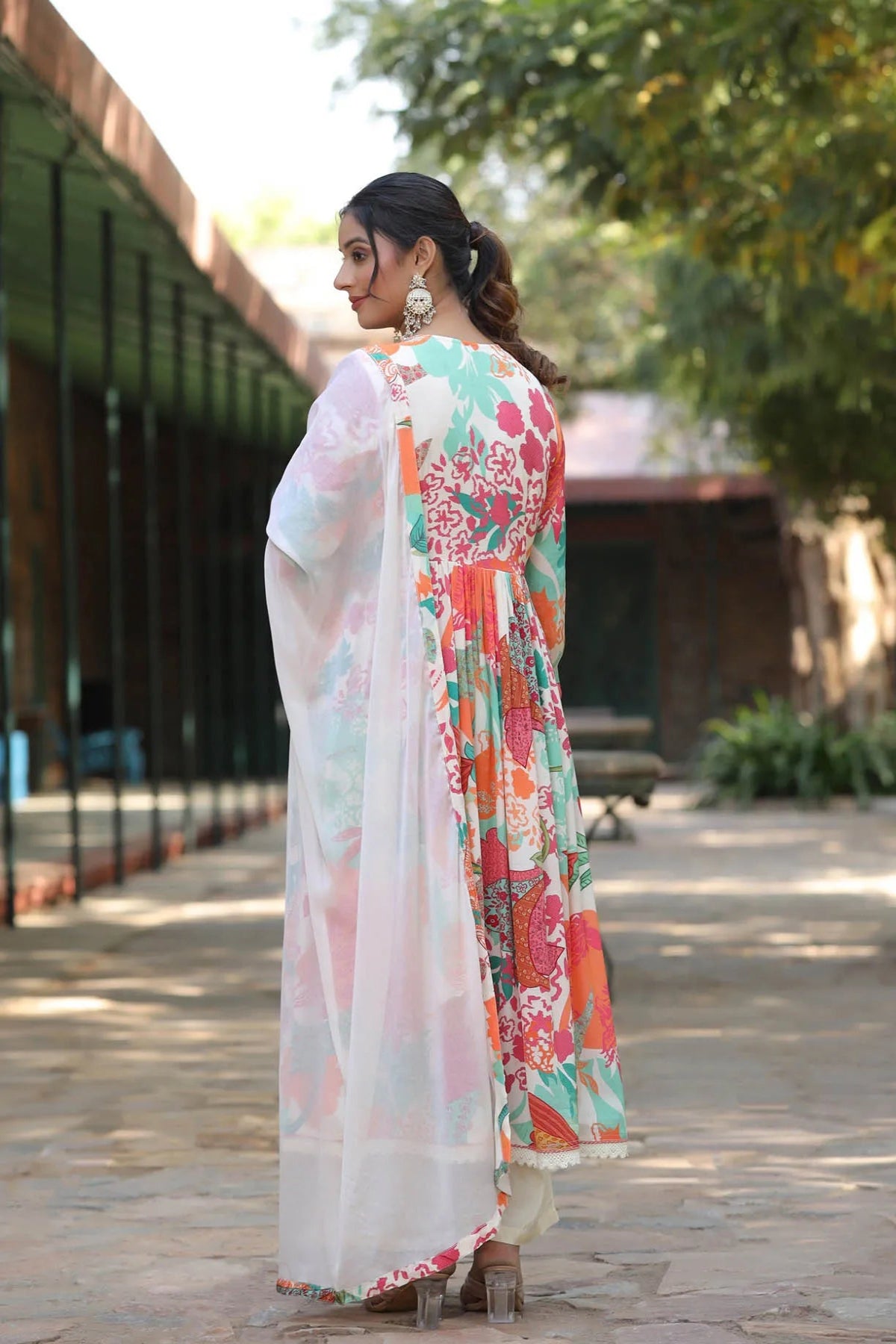 Woman wearing a colorful floral dress with a sheer dupatta in an outdoor setting.