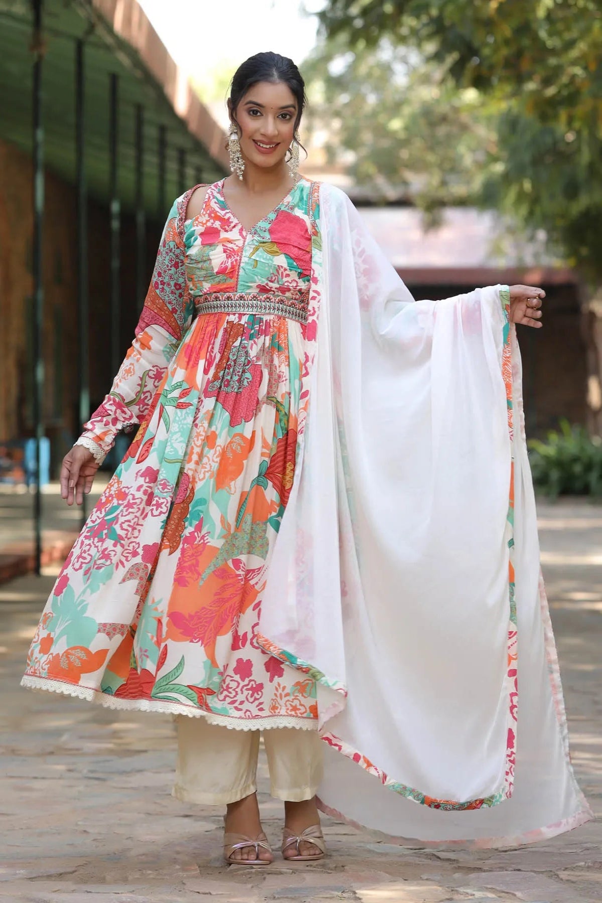 Woman wearing a colorful floral dress with a white dupatta outdoors.