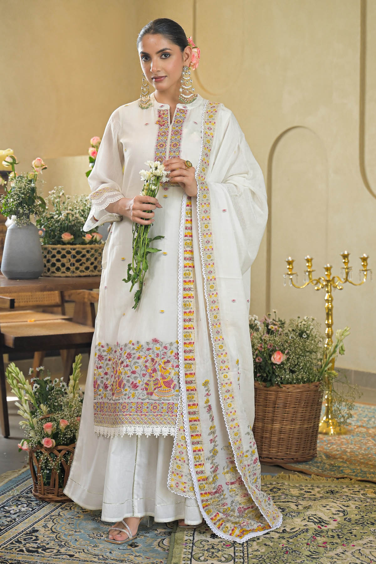 Woman in a traditional outfit with floral patterns in an elegant indoor setting.