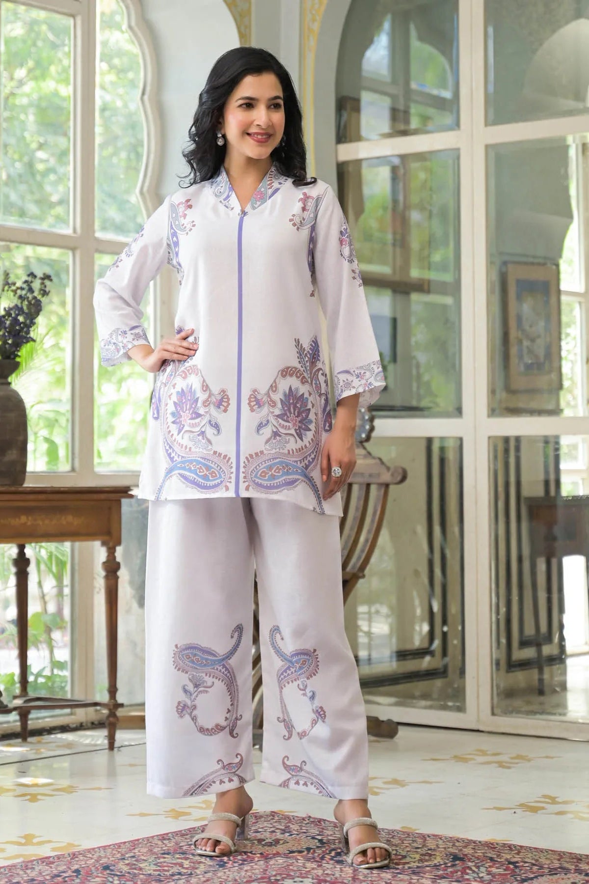 Woman wearing a white embroidered outfit in a room with large windows.