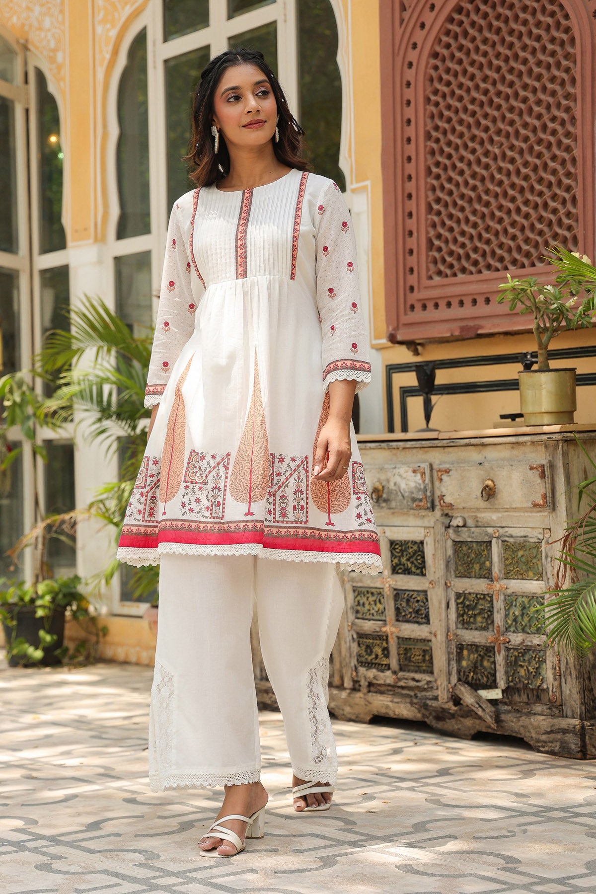 Woman wearing a white embroidered outfit with red details in an outdoor setting.