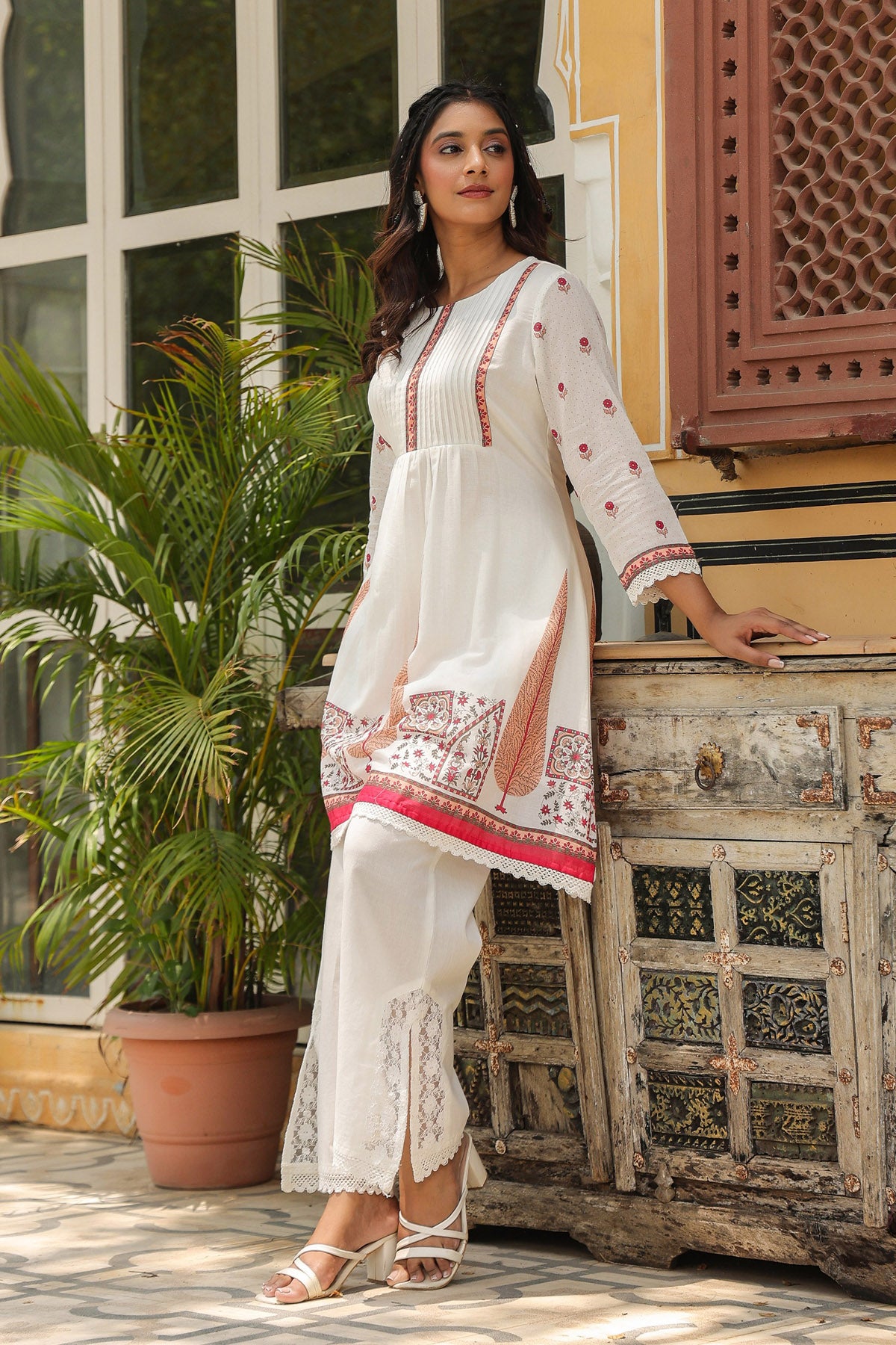 Woman in a white and red traditional outfit standing in front of a decorative wooden cabinet.
