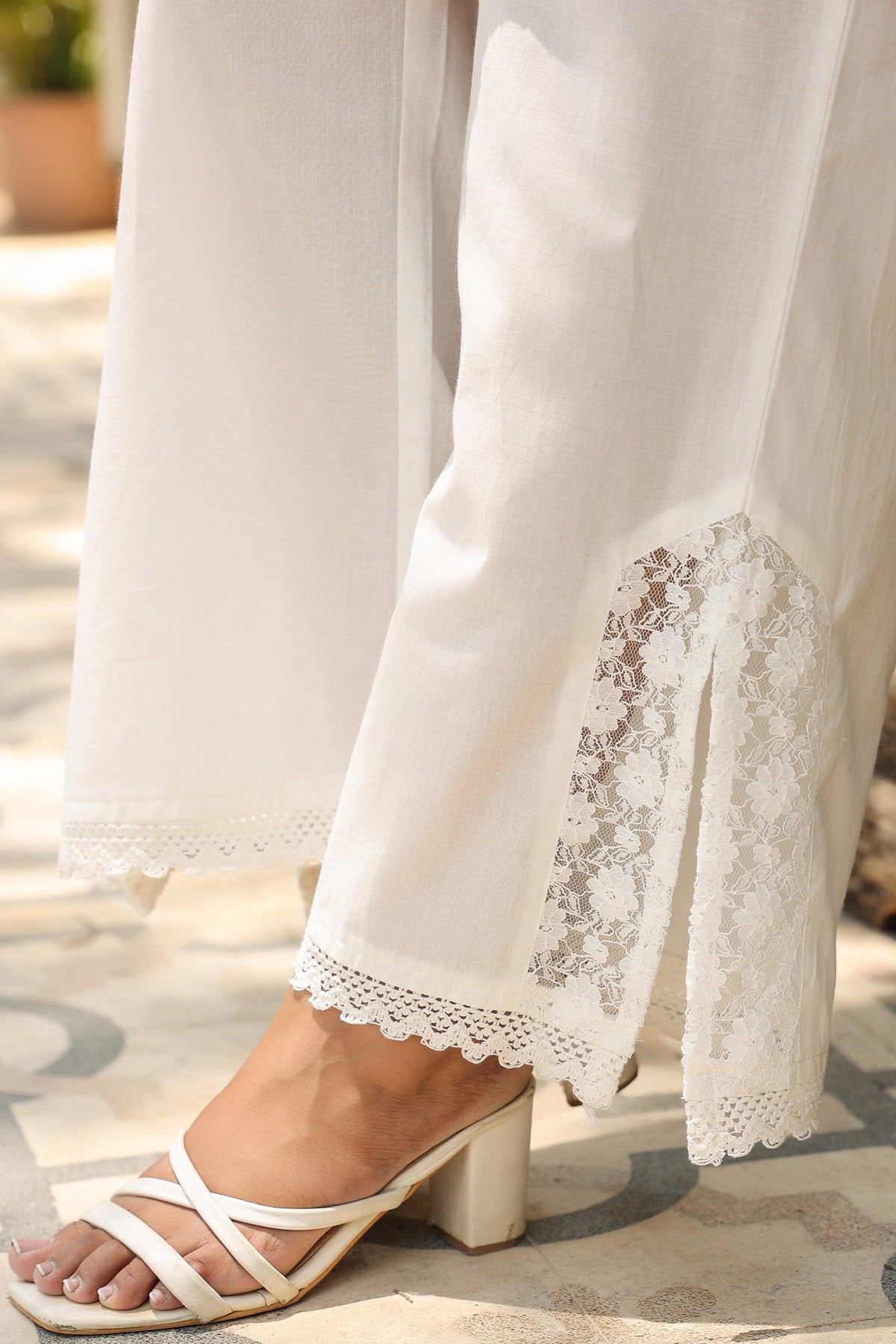 White lace-trimmed pants with a sandal on a blurred outdoor background