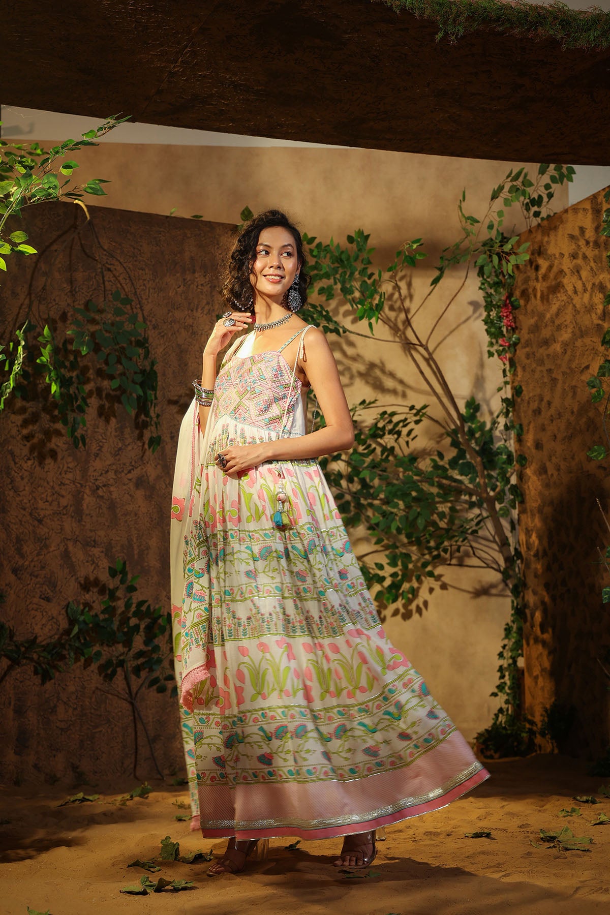 Woman in a floral dress standing in a natural setting with plants and a beige wall.