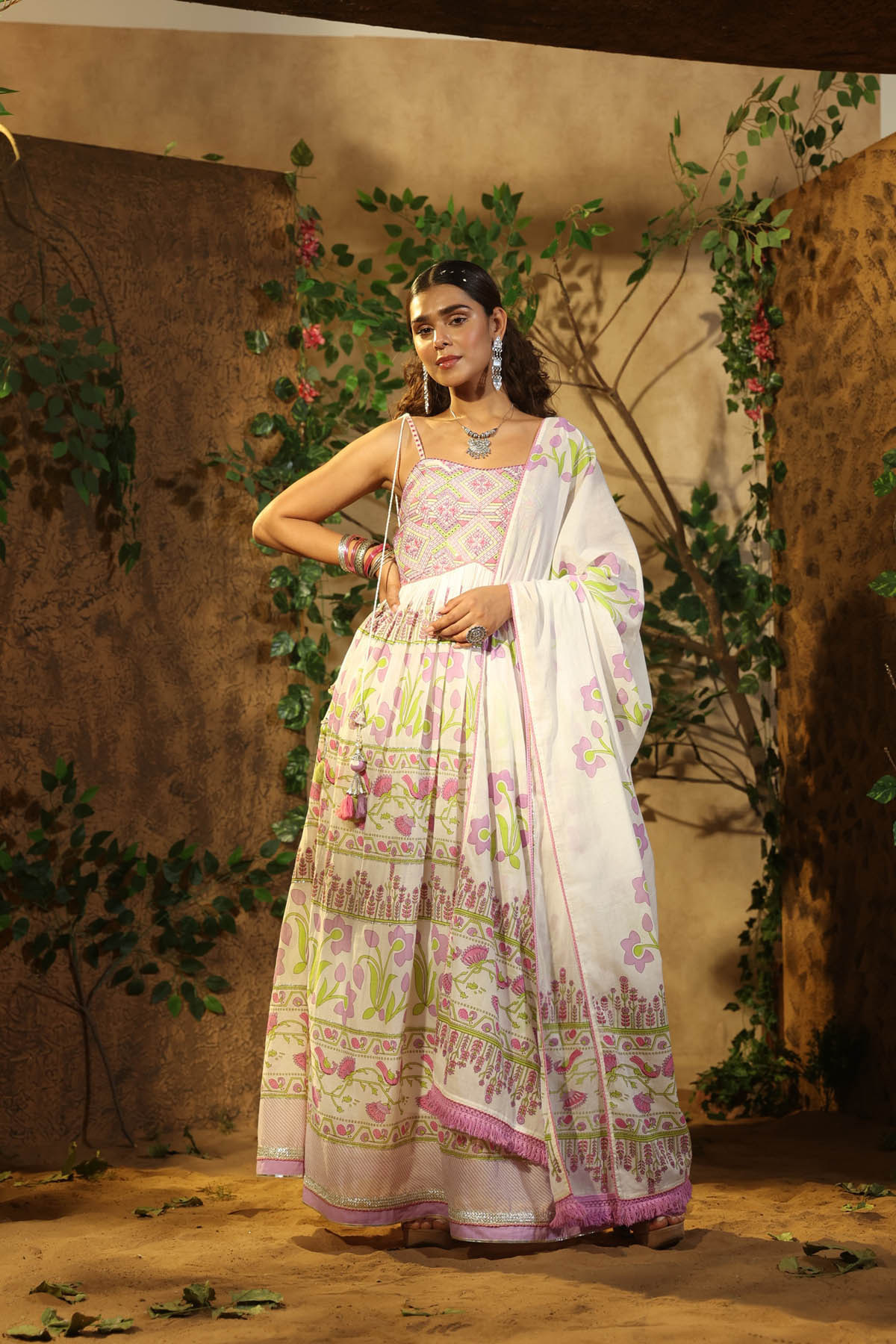 Woman in a traditional outfit with a floral pattern standing against a decorative background.