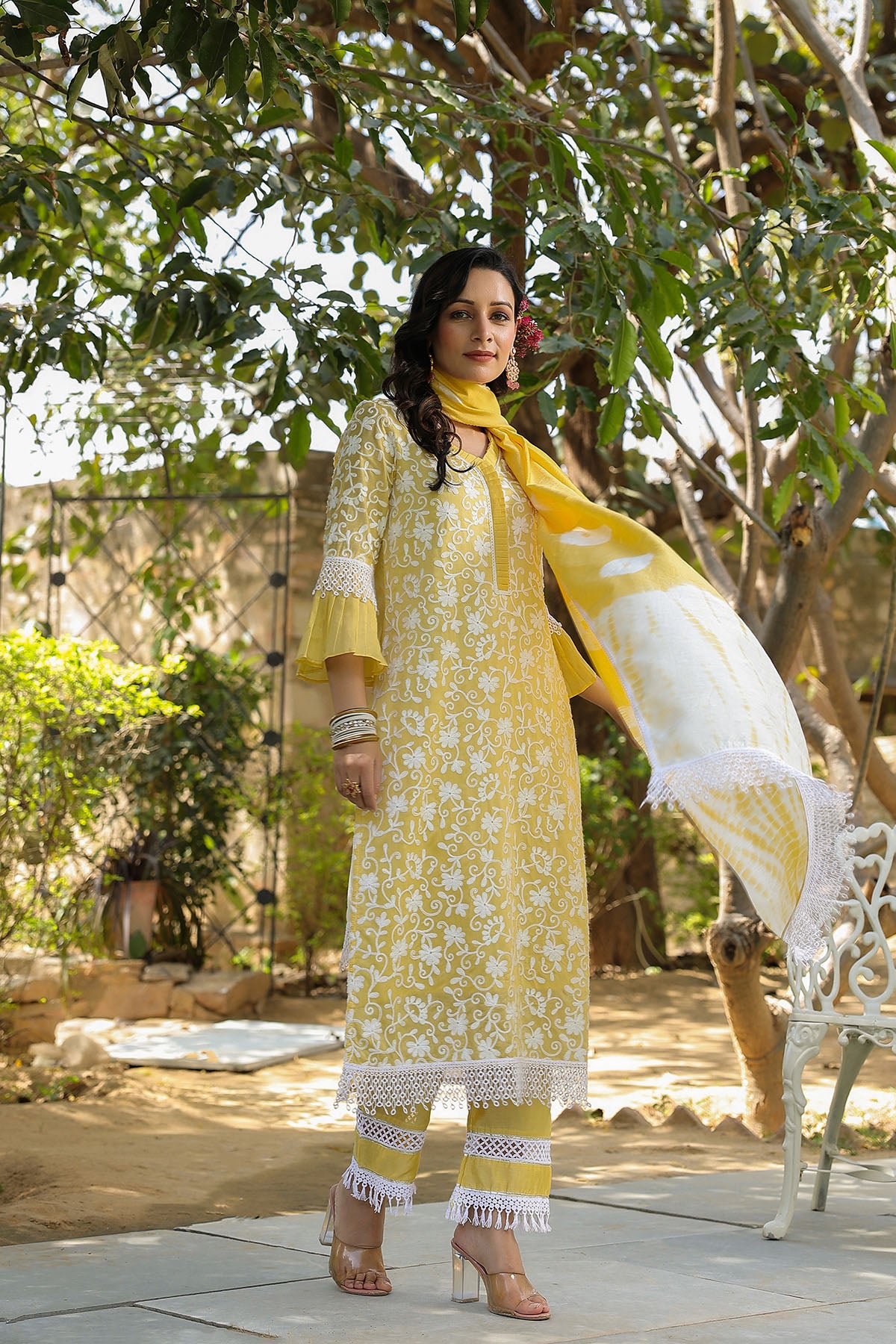 Woman in a yellow and white traditional outfit with a scarf, standing outdoors.