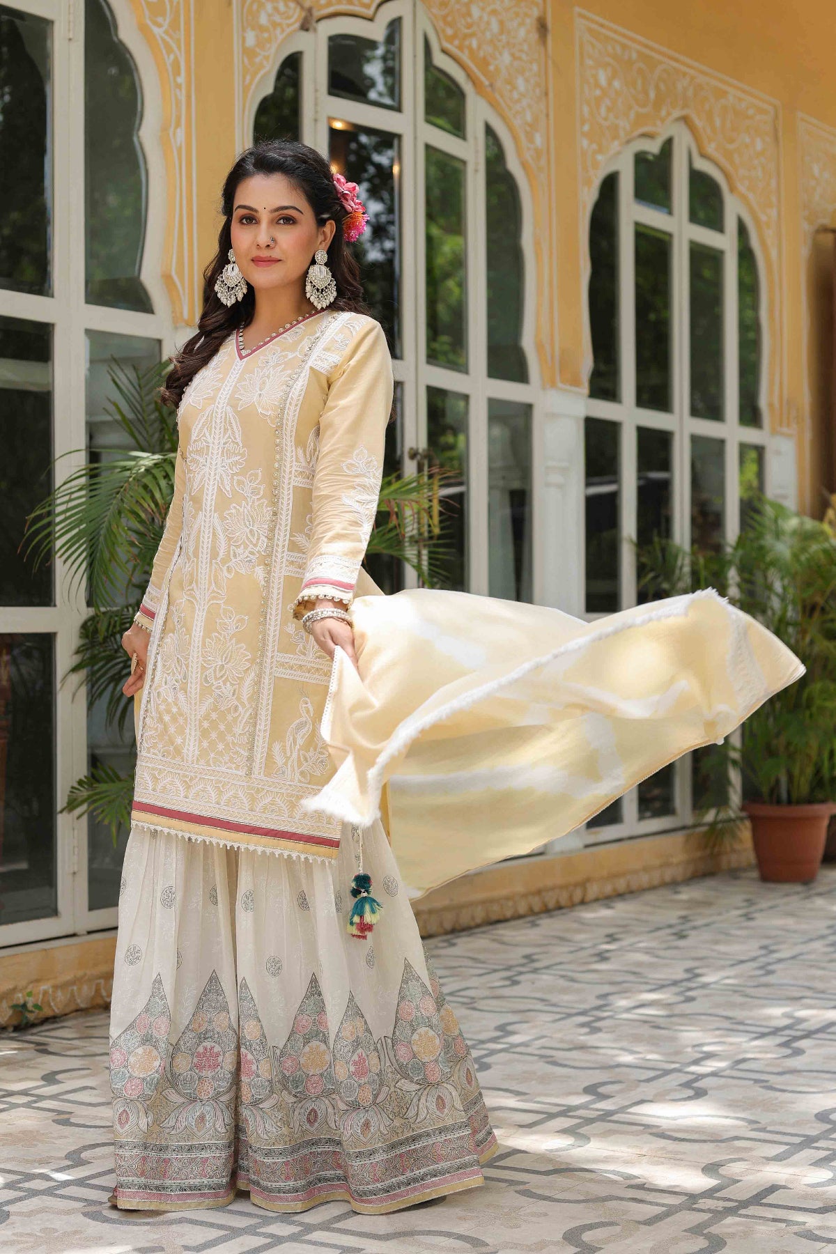 Woman in a traditional outfit standing in front of a decorative building with large windows.
