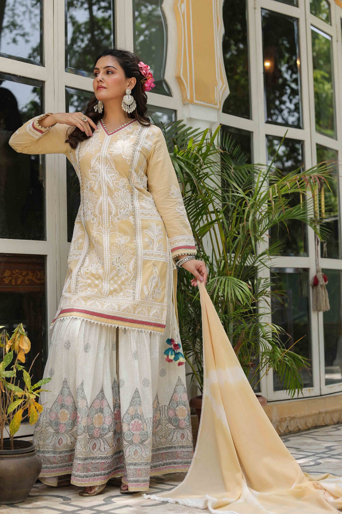 Woman in traditional outfit with floral decorations, standing indoors with plants in the background