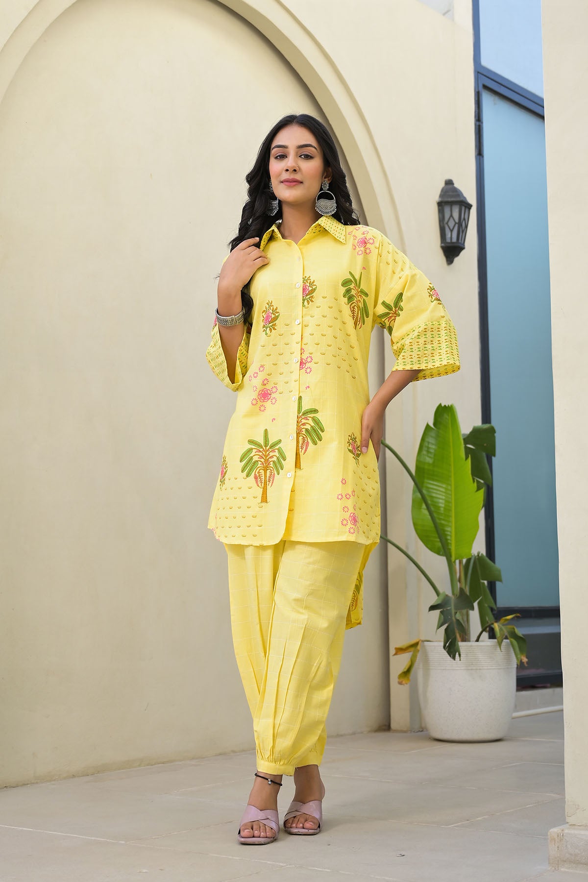 Woman wearing a yellow outfit with floral patterns standing in front of a white archway.