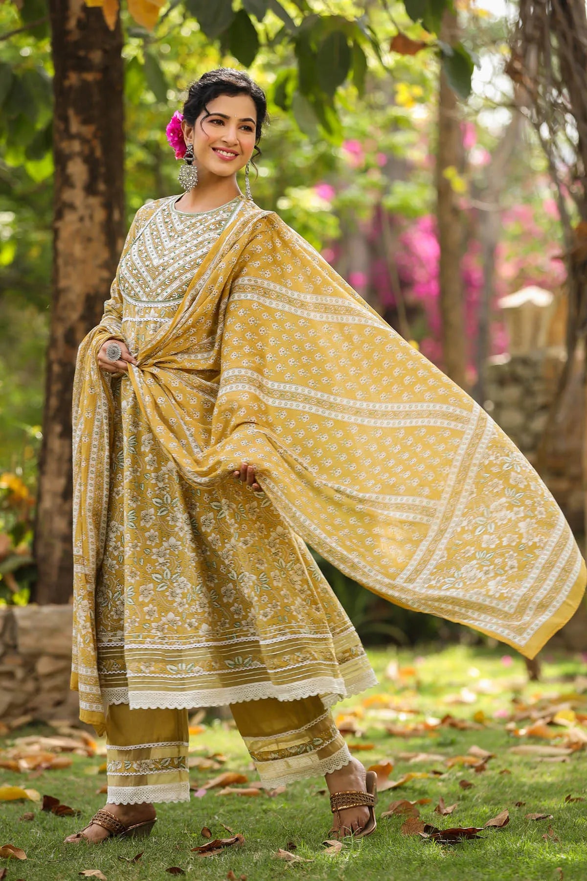 Woman in a yellow traditional outfit standing outdoors with greenery in the background