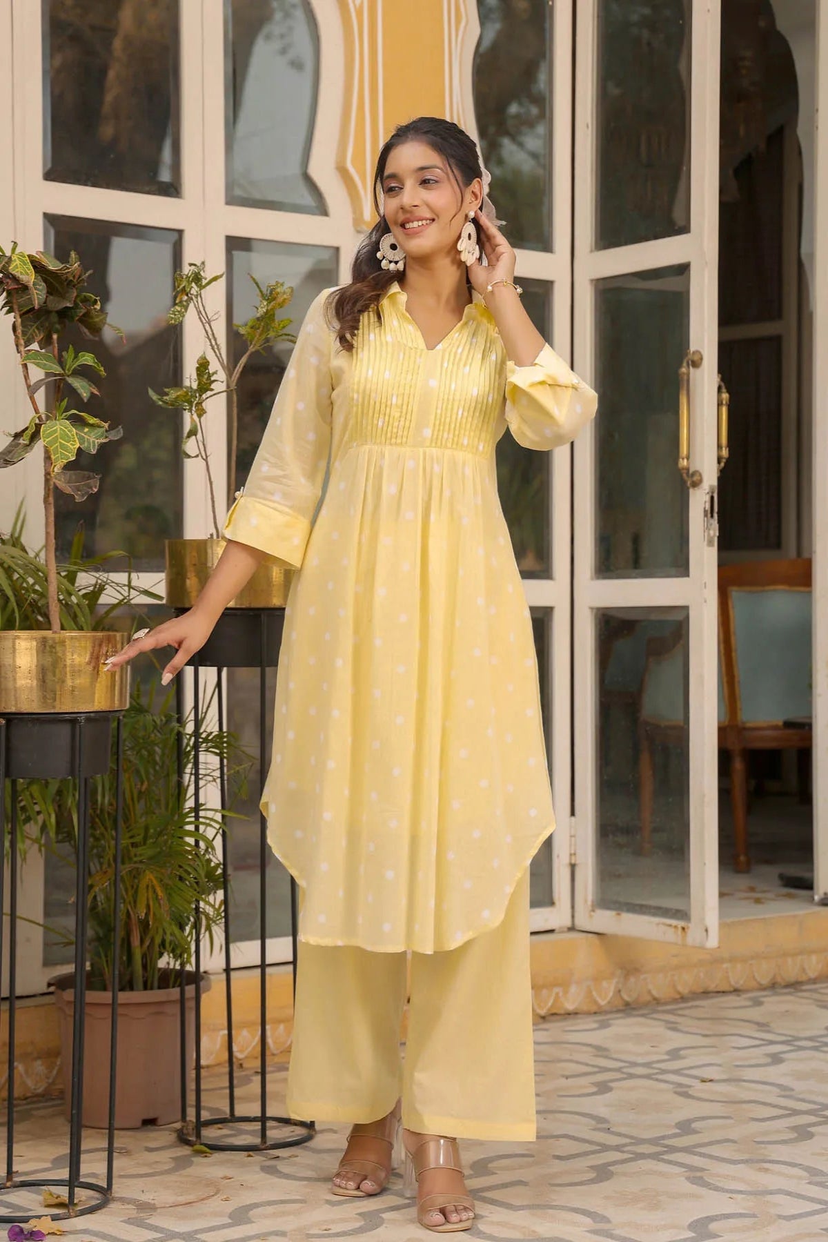 Woman in a yellow outfit standing in front of a glass door with plants around.