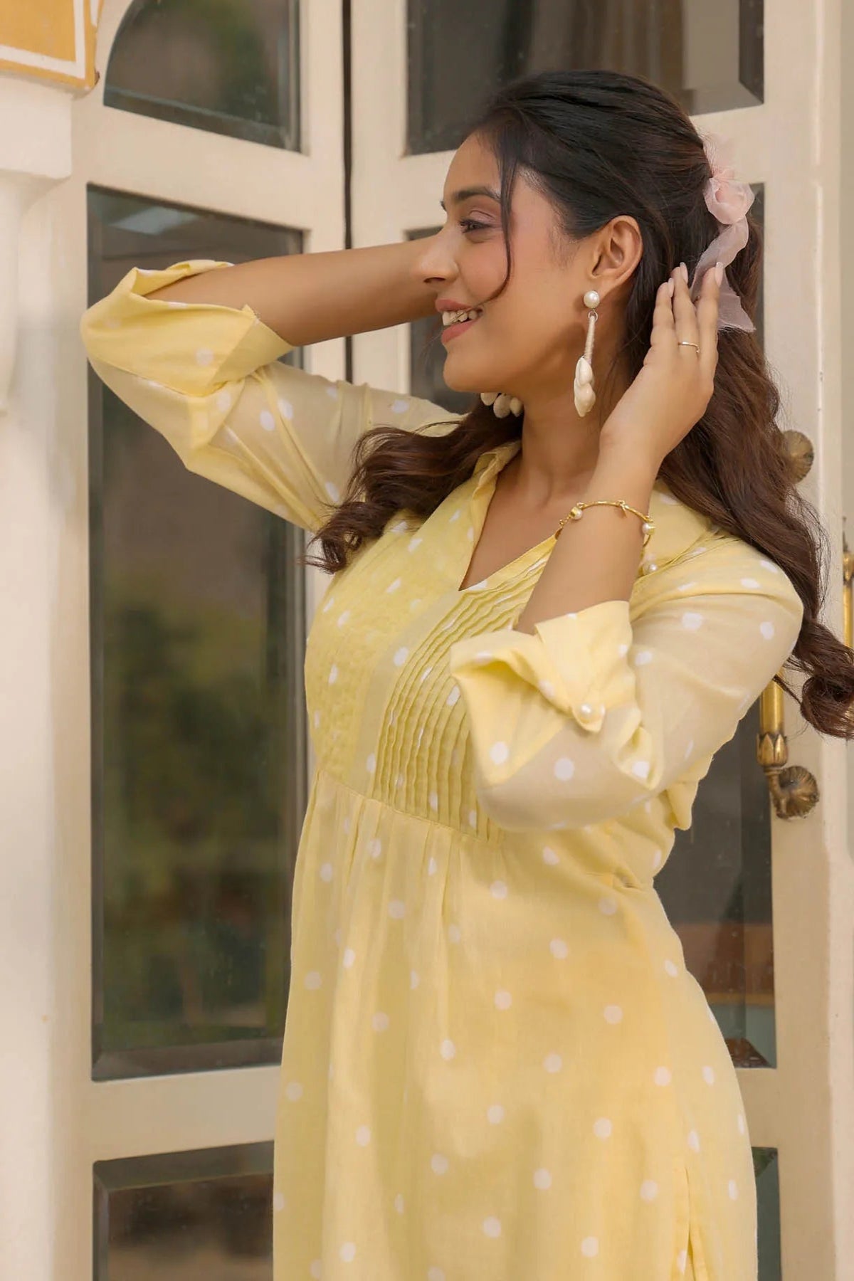 Woman in a yellow polka dot dress standing indoors with a blurred background