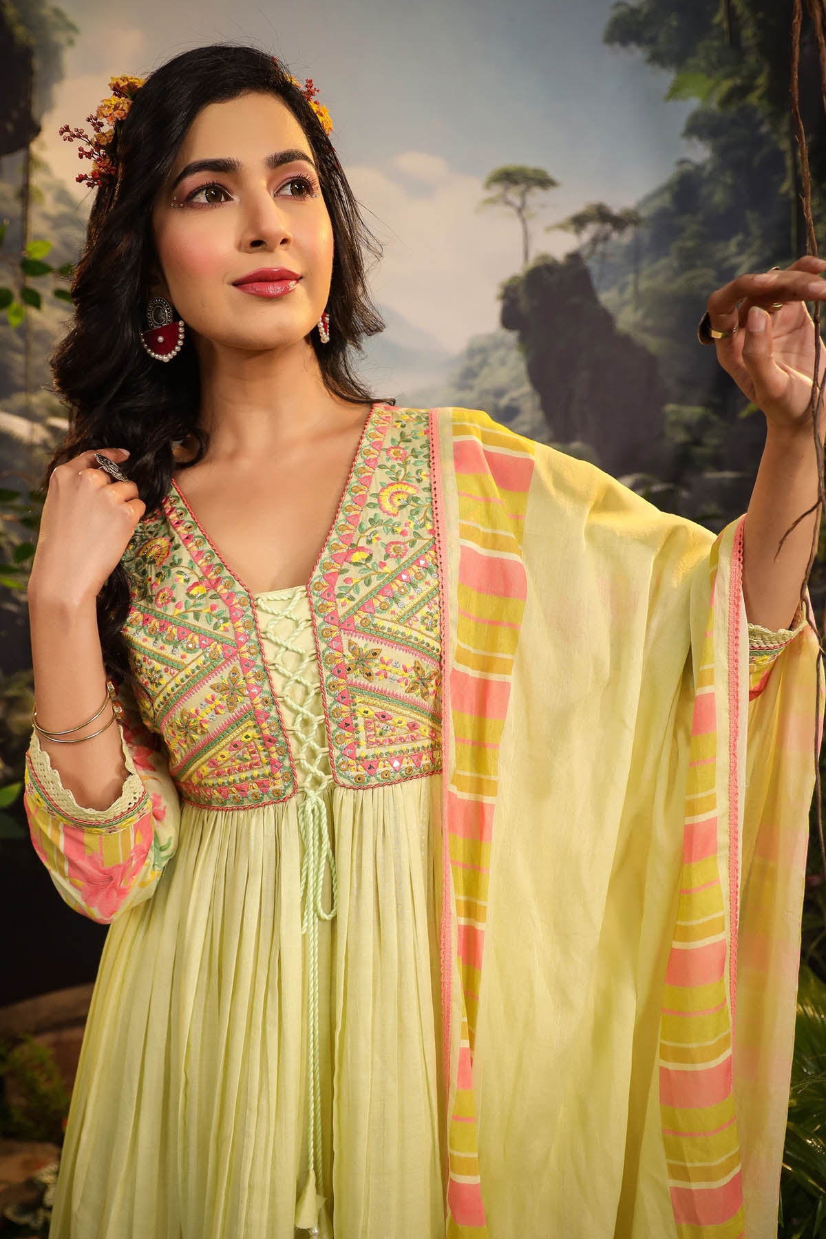 Woman wearing a traditional outfit with a colorful top and light yellow dupatta against a natural background.
