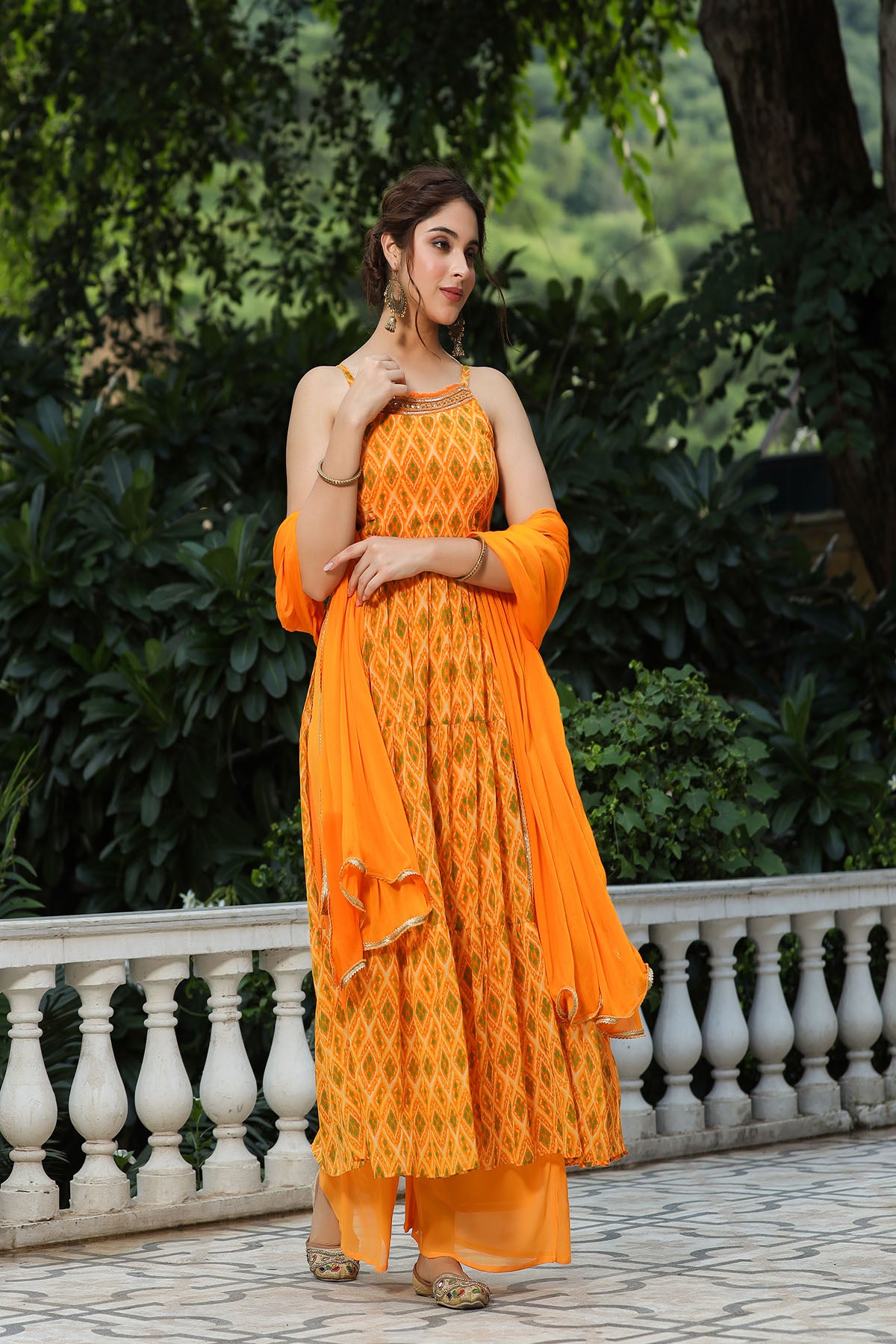 Woman in an orange dress standing outdoors with greenery in the background