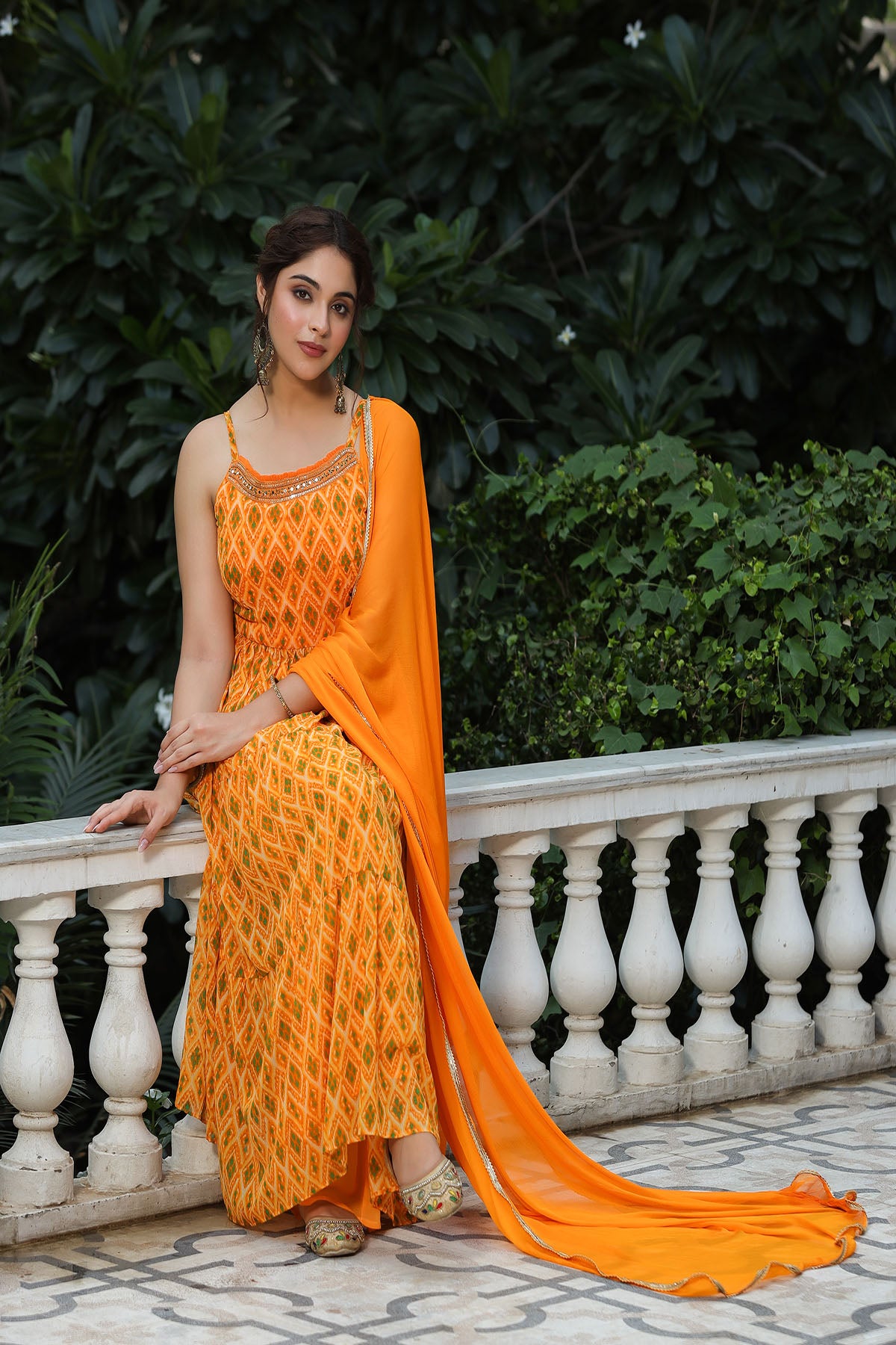 Woman in an orange saree with a floral pattern standing outdoors.