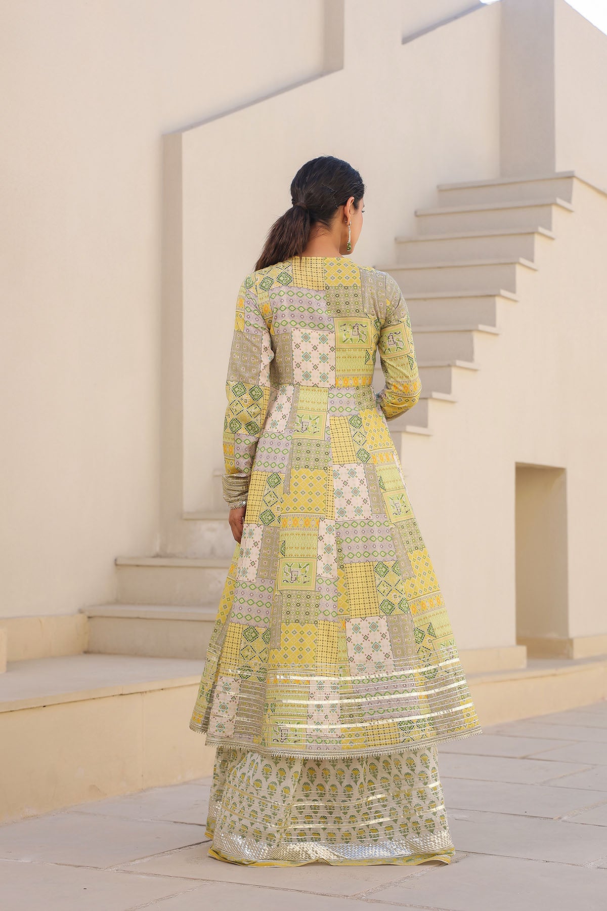 Woman in a patterned dress standing on steps with a neutral background
