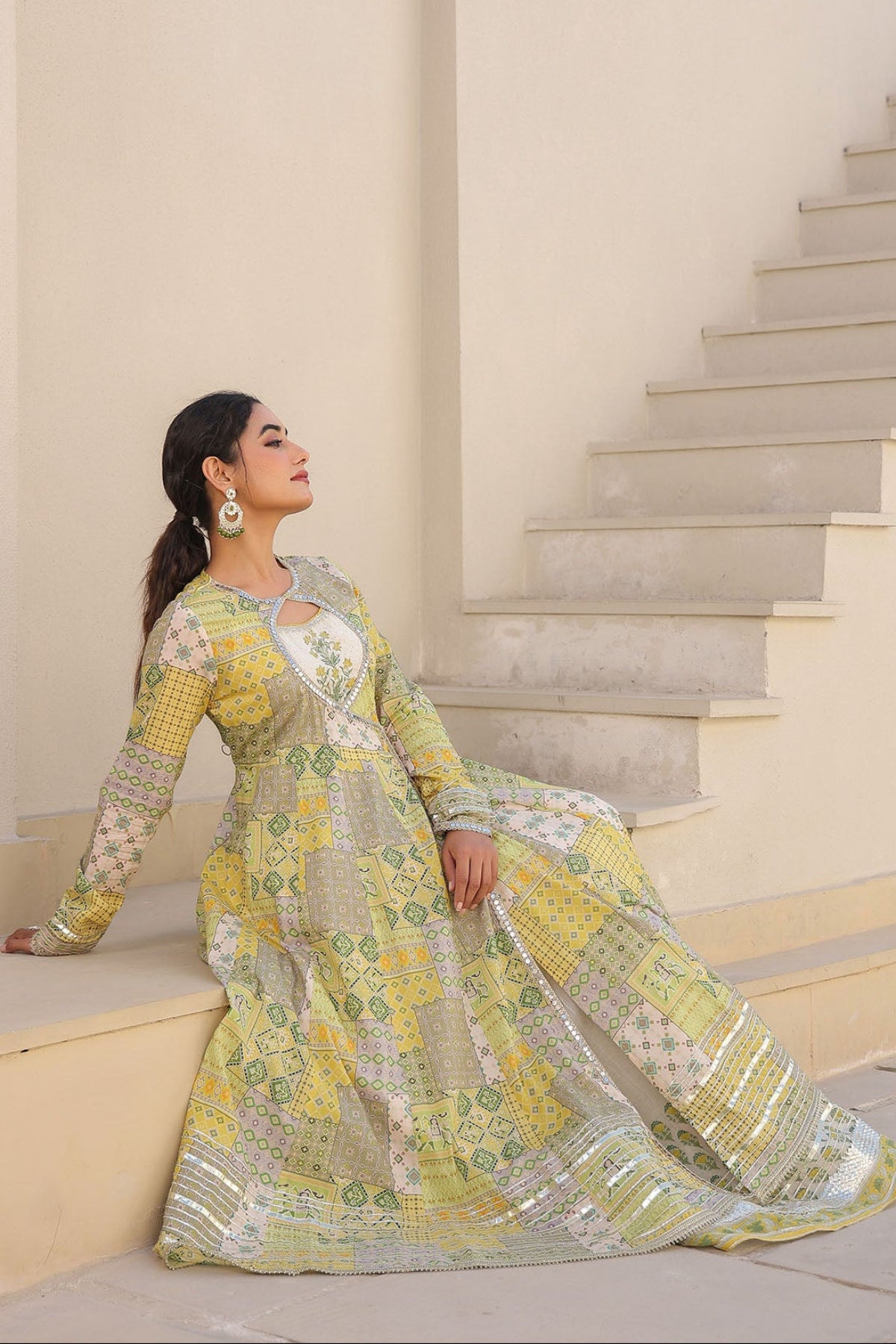 Woman in a yellow and green patterned dress standing on a staircase.