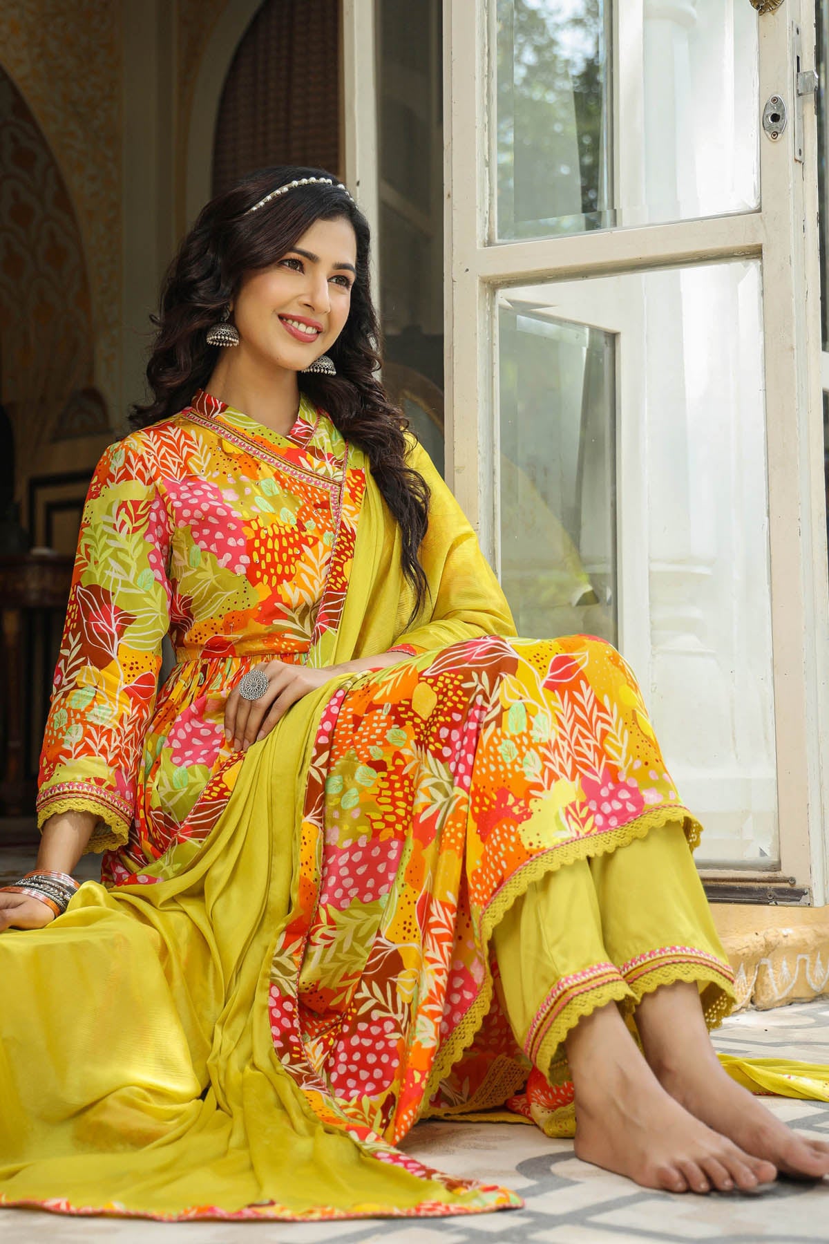Woman in a colorful traditional outfit sitting in a well-lit room.