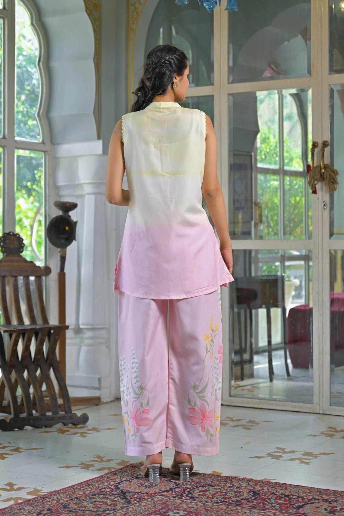 Woman in a light-colored outfit standing in a room with large windows.