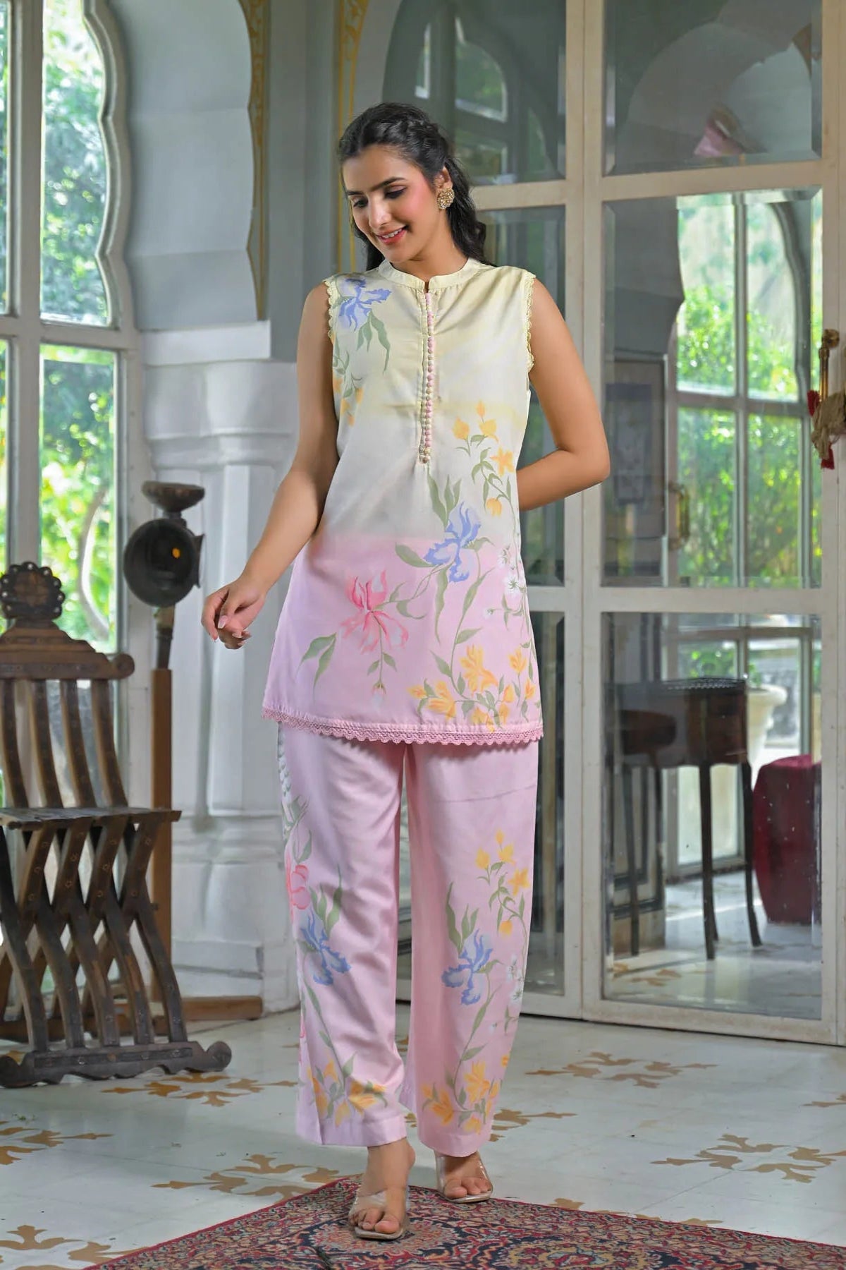 Woman wearing a pink floral outfit in a room with large windows.