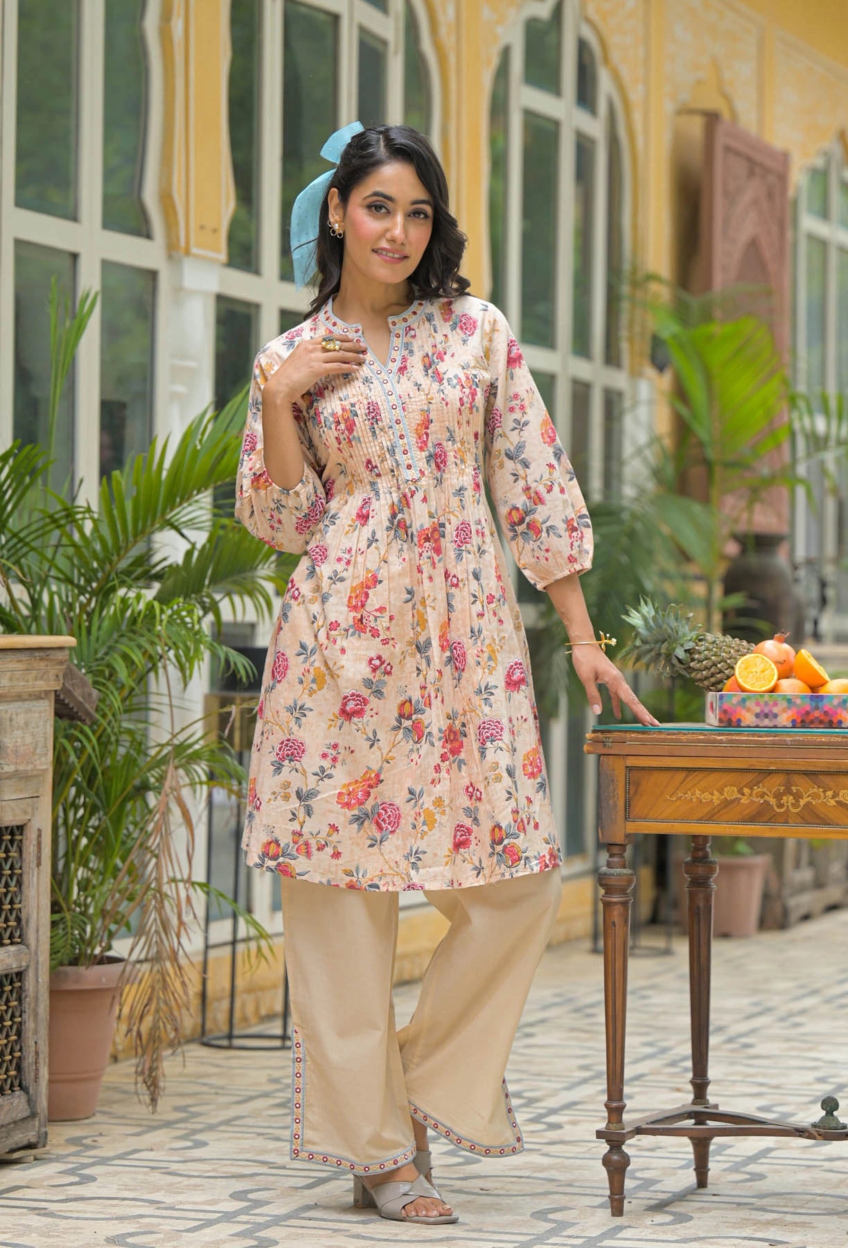 Woman in a floral dress standing outdoors with a table and plants in the background