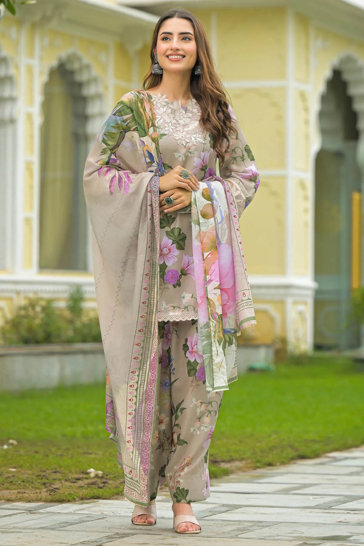 Woman in traditional outfit with floral patterns standing in front of a yellow building.