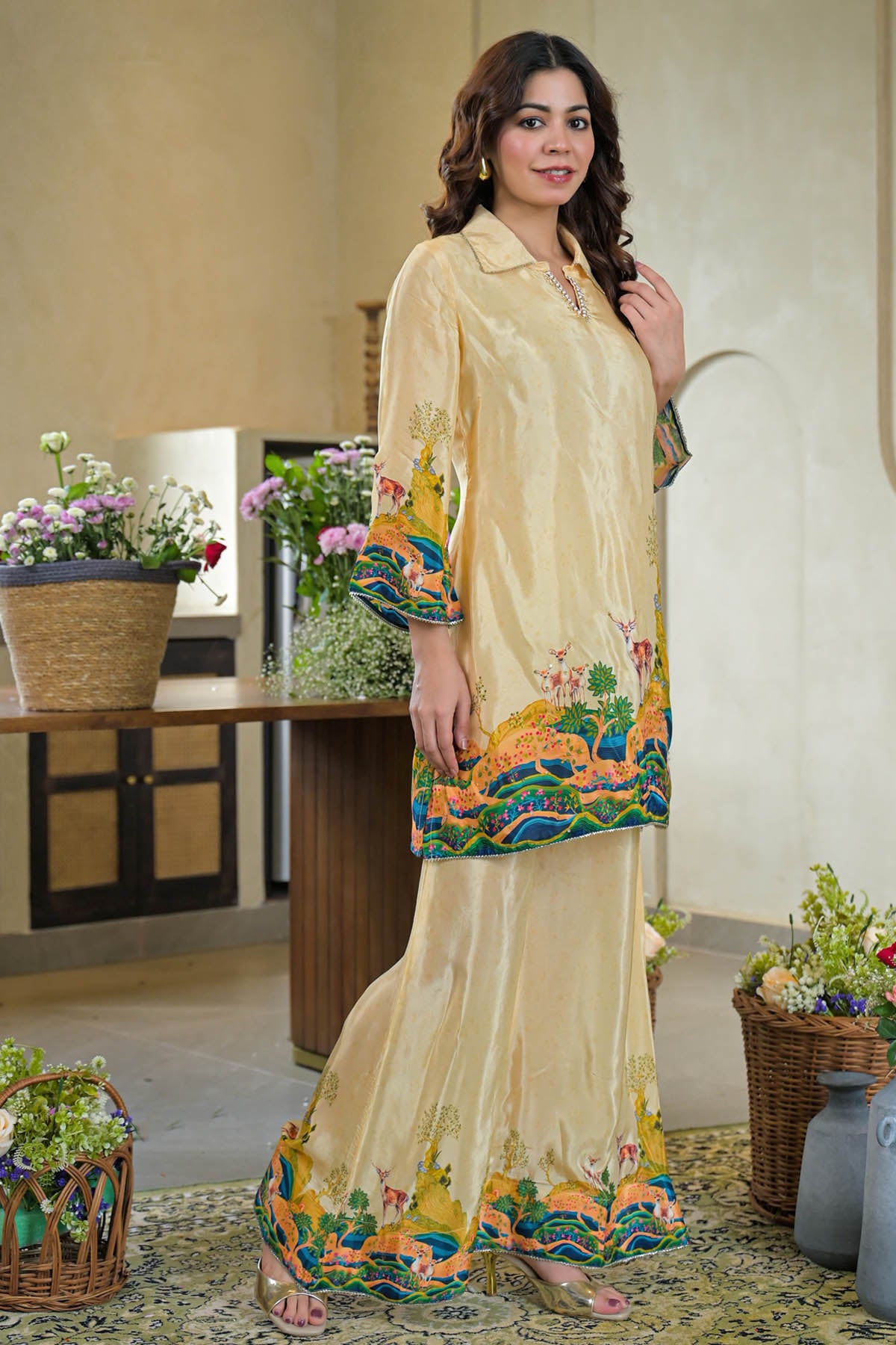 Woman wearing a beige and floral dress in an indoor setting with decorative plants.