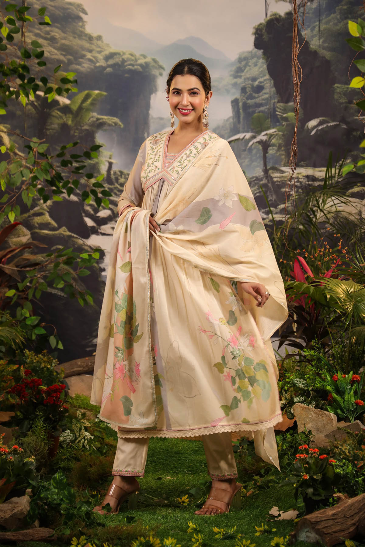 Woman in traditional attire standing in a natural setting with greenery and mountains.