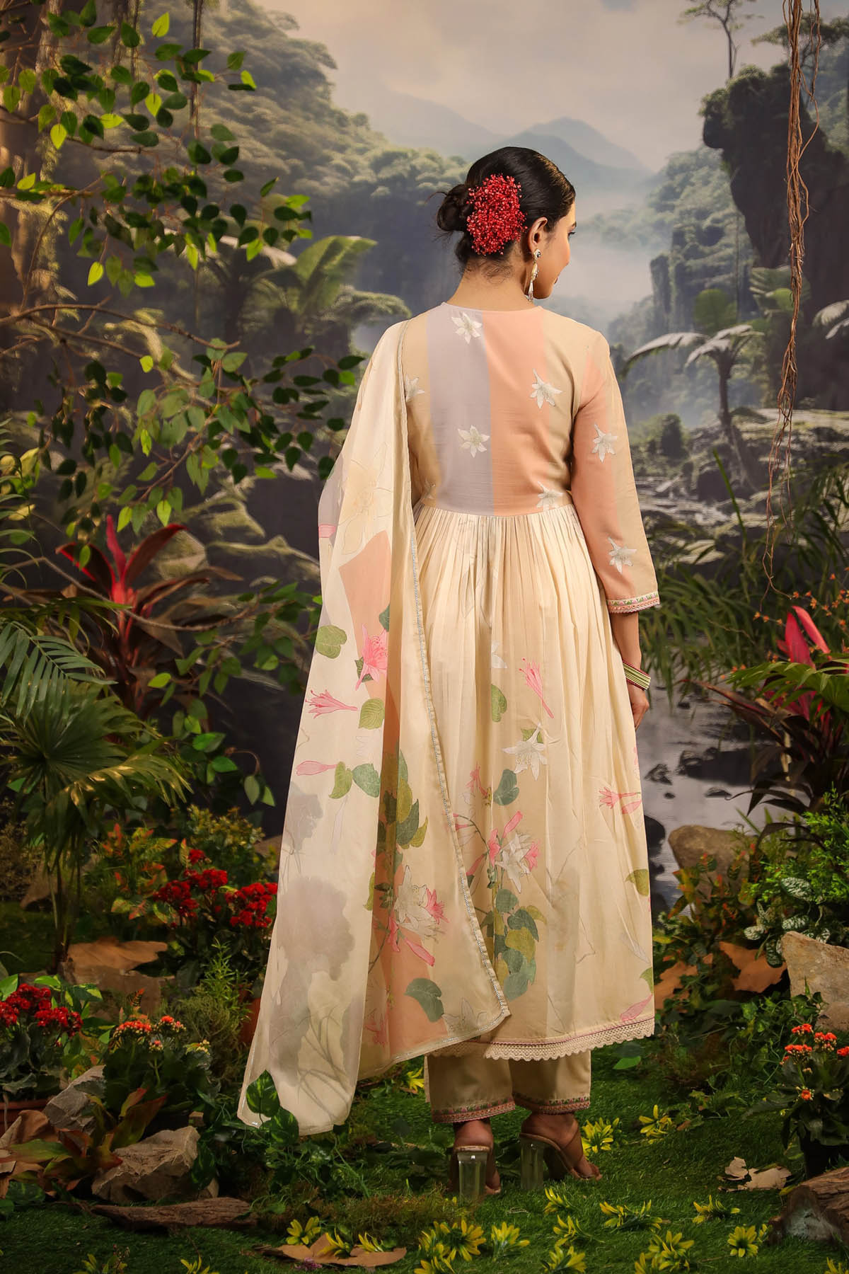 Woman in a floral dress standing in a lush, tropical setting with mountains in the background.
