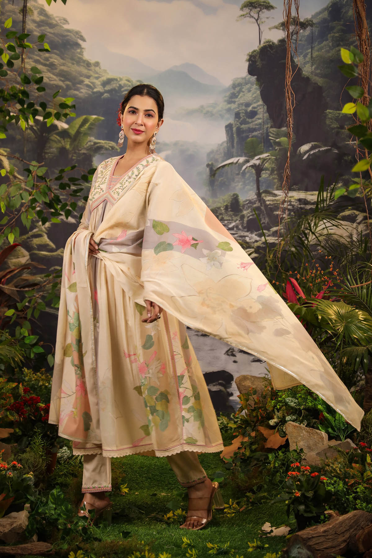 Woman in a traditional outfit standing in a natural setting with trees and mountains.