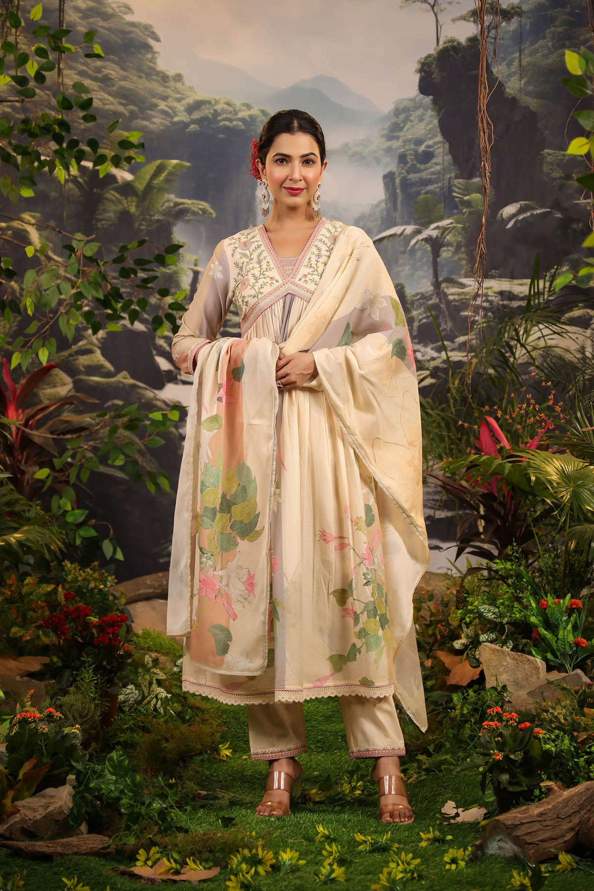 Woman in traditional attire standing in a natural setting with greenery and mountains.