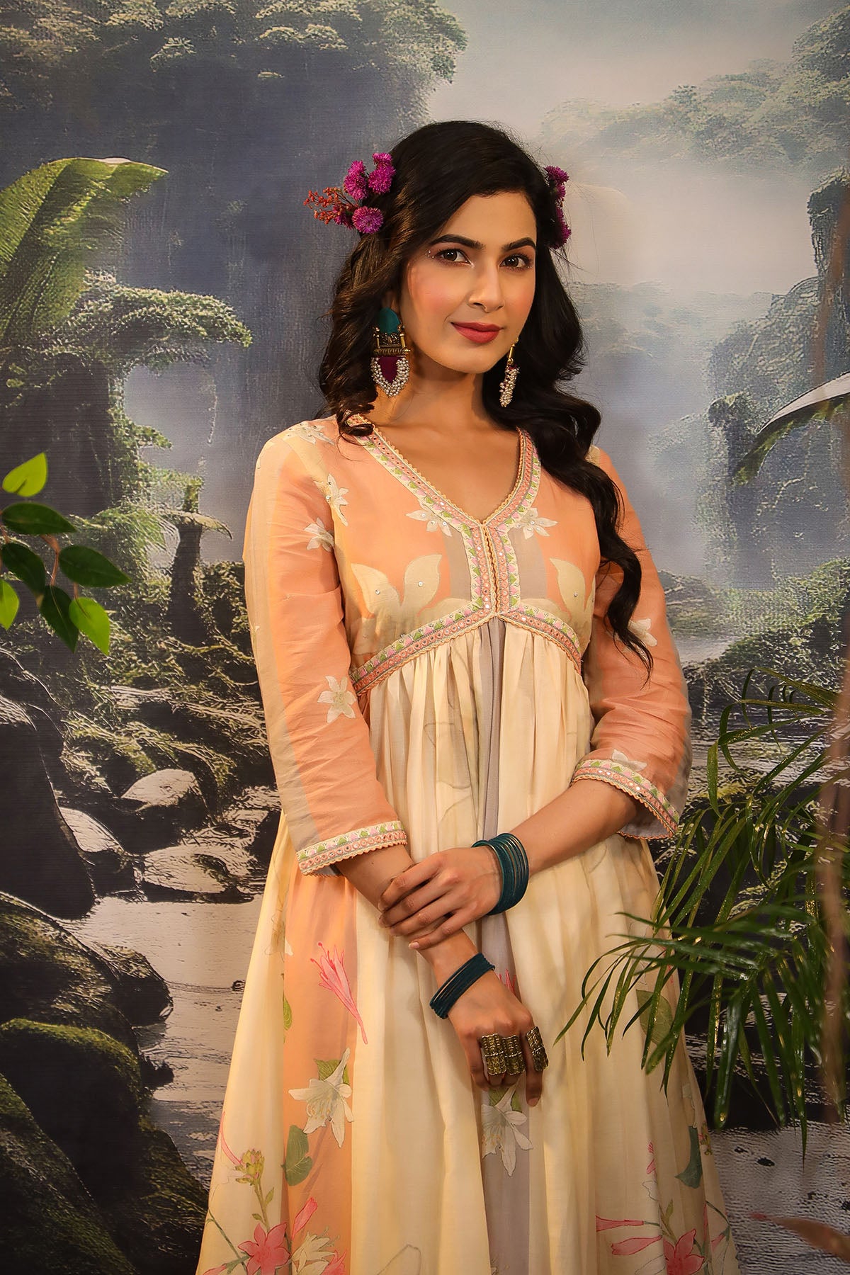 Woman in a peach and white traditional outfit standing in front of a scenic background with trees and rocks.