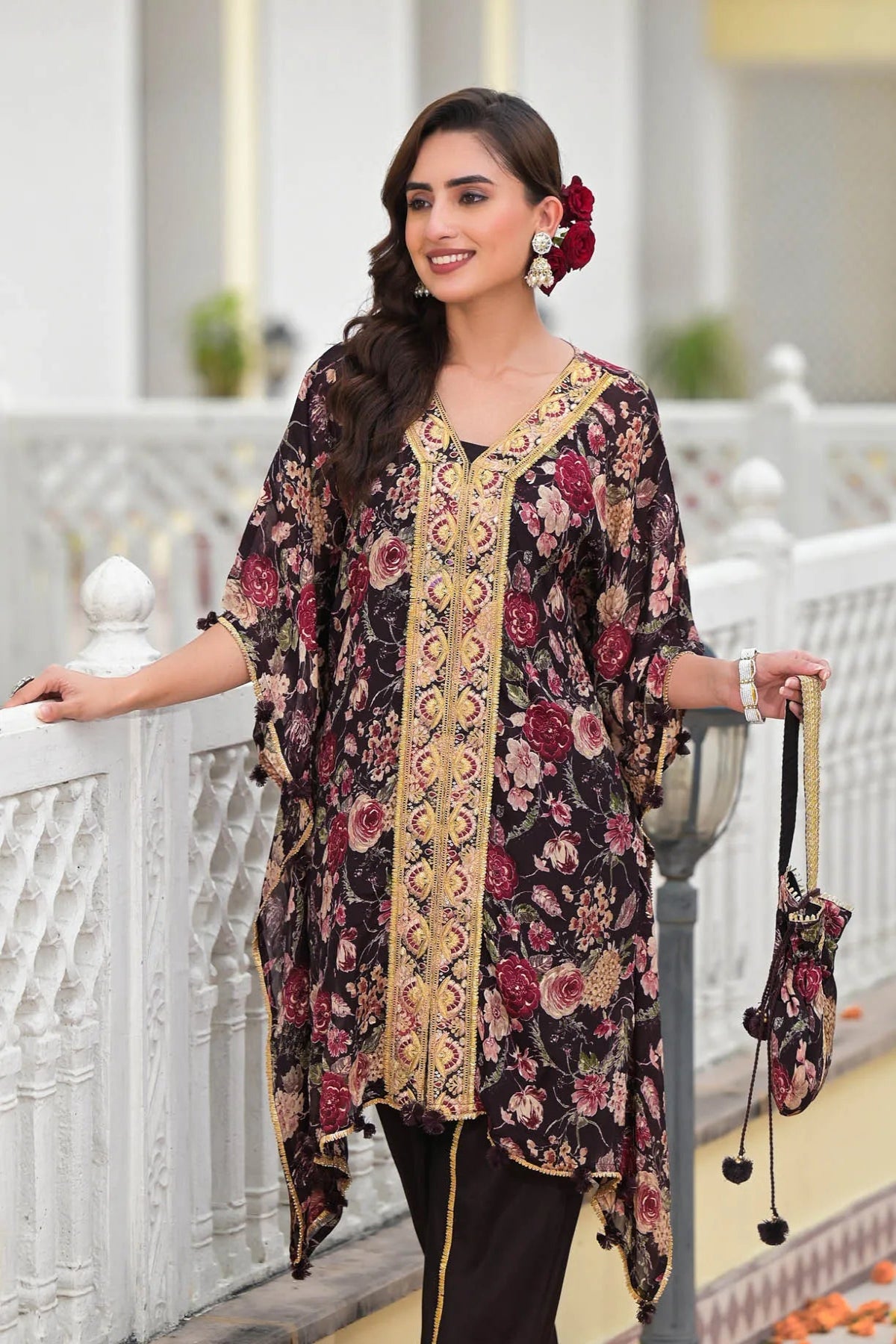 Woman wearing a floral and embroidered dress standing on a decorative balcony.