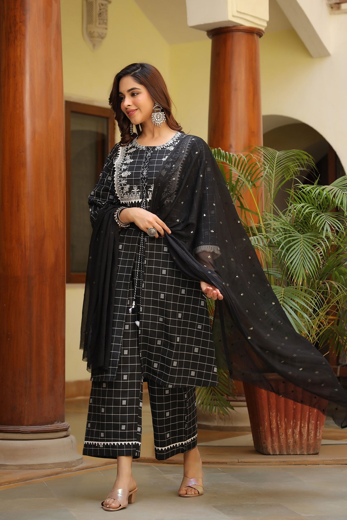 Woman in a black and white traditional outfit standing in an indoor setting with plants.