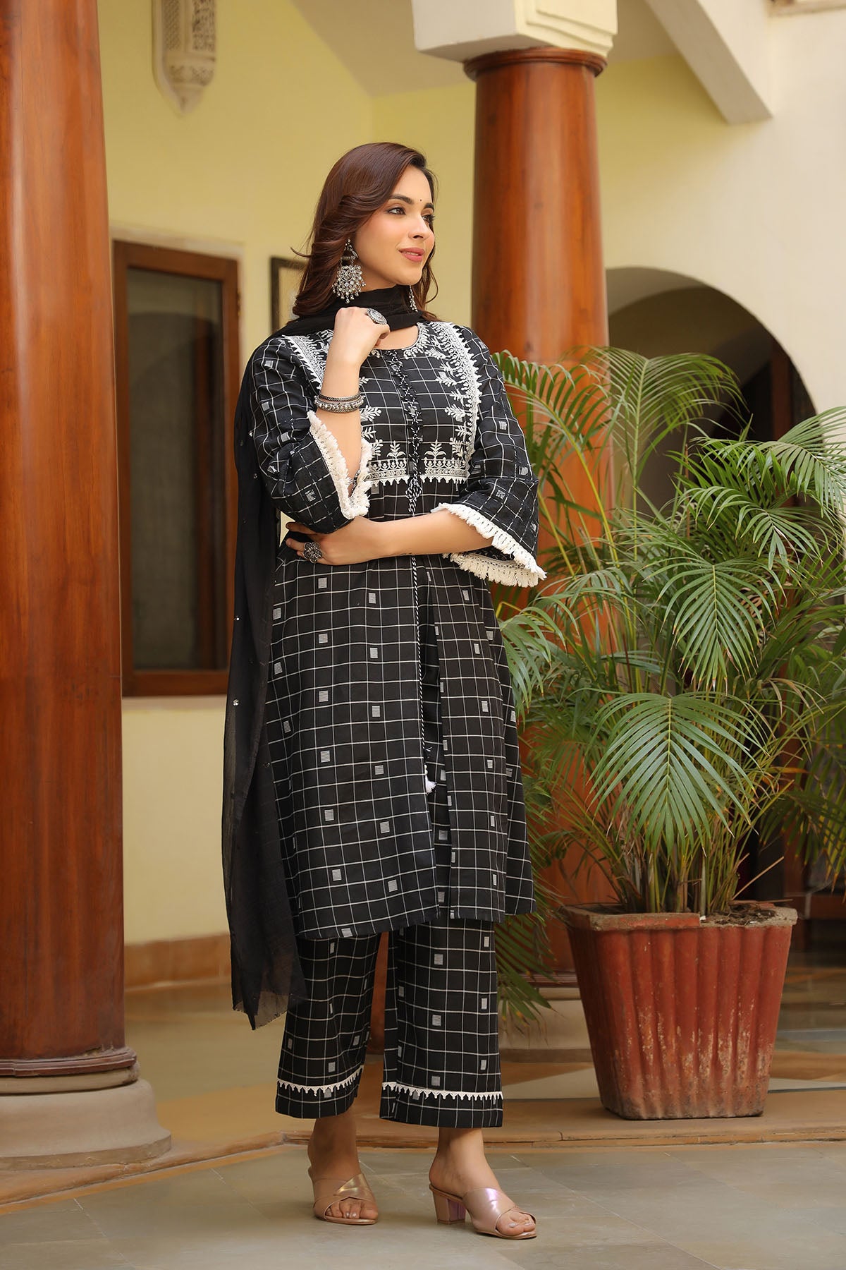 Woman in a black and white traditional outfit standing indoors with plants in the background