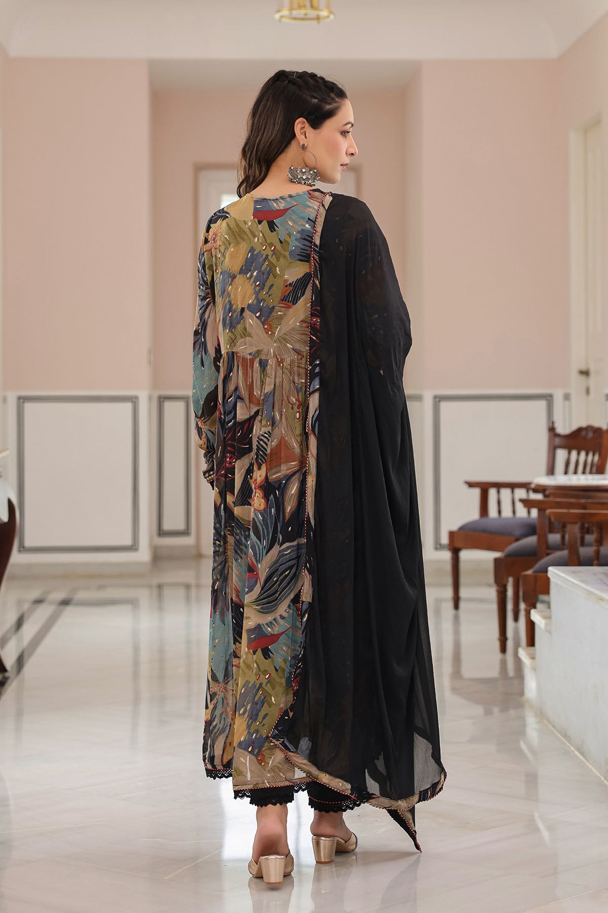 Woman wearing a floral shawl over a black outfit in a room with pink walls and wooden furniture.